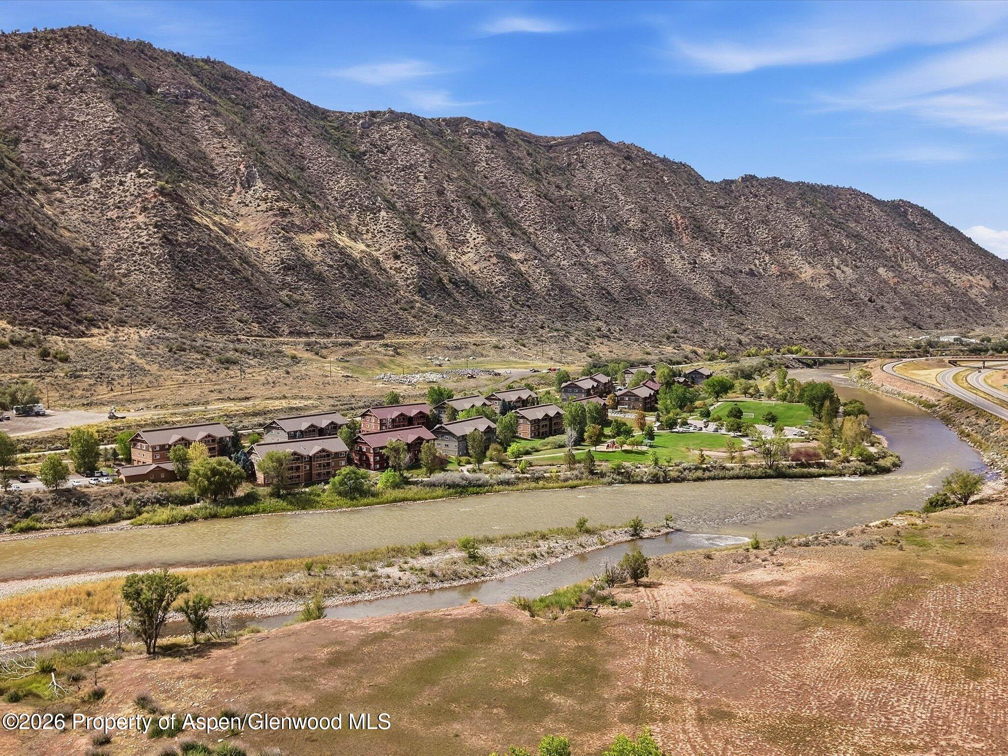 Aerial view of riverside homes beside a winding river, with dry mountains behind.