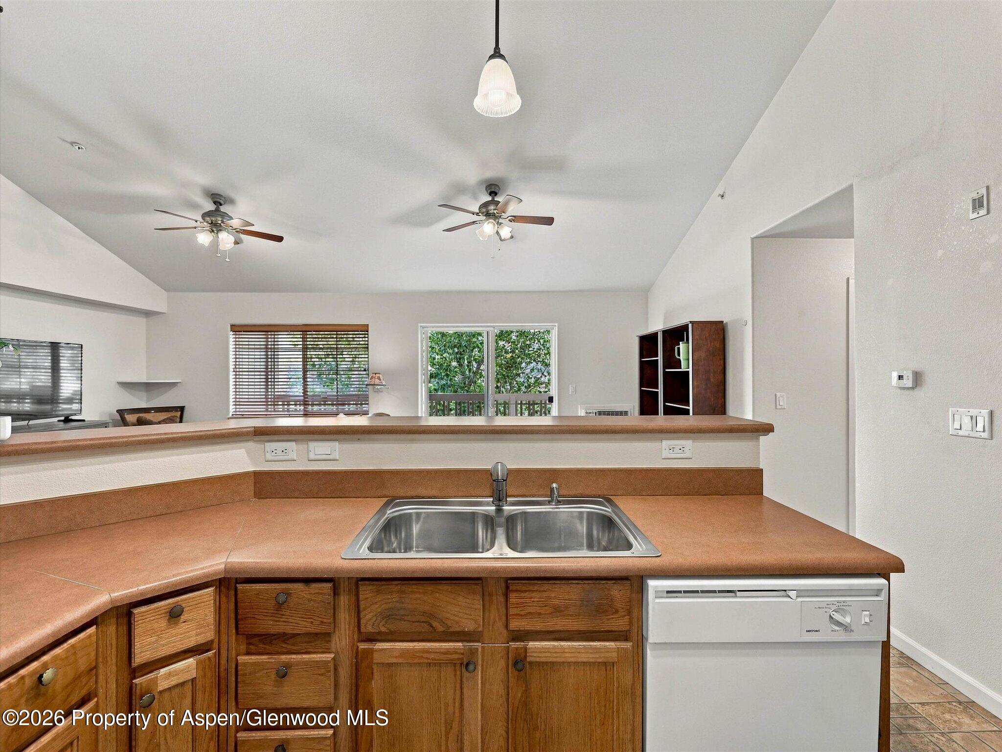 Kitchen with a double-basin sink, terracotta countertops, wood cabinets, and an open living area beyond the bar.