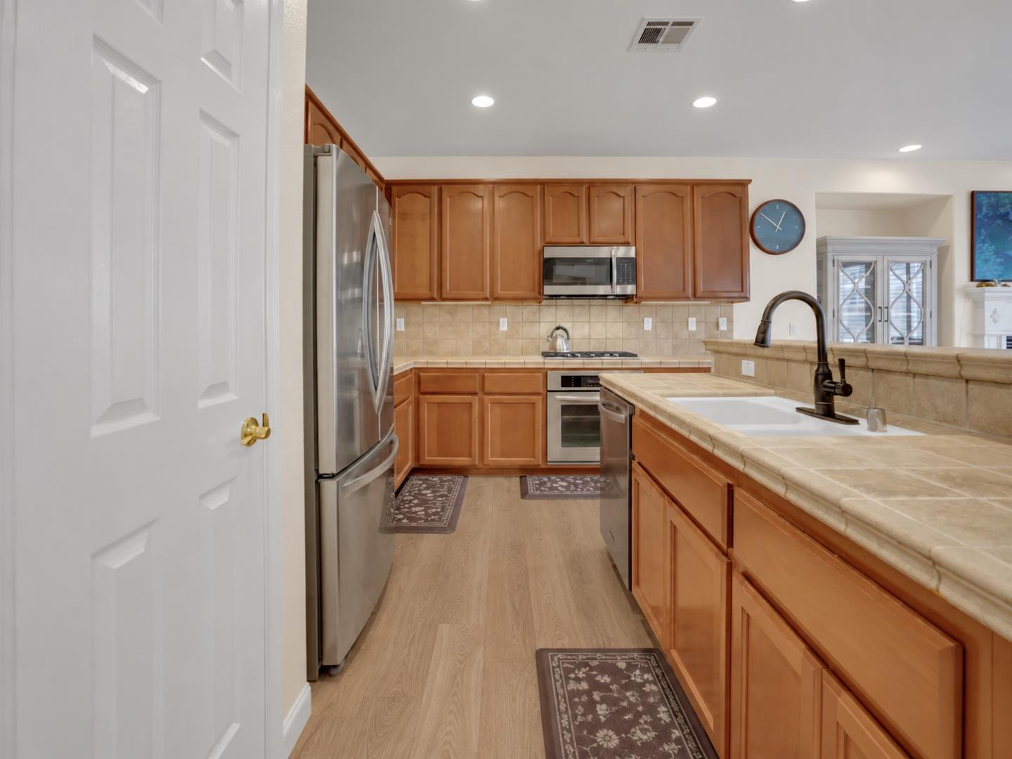 Kitchen with warm wood cabinets, stainless steel appliances, and a large tiled peninsula with a white sink.