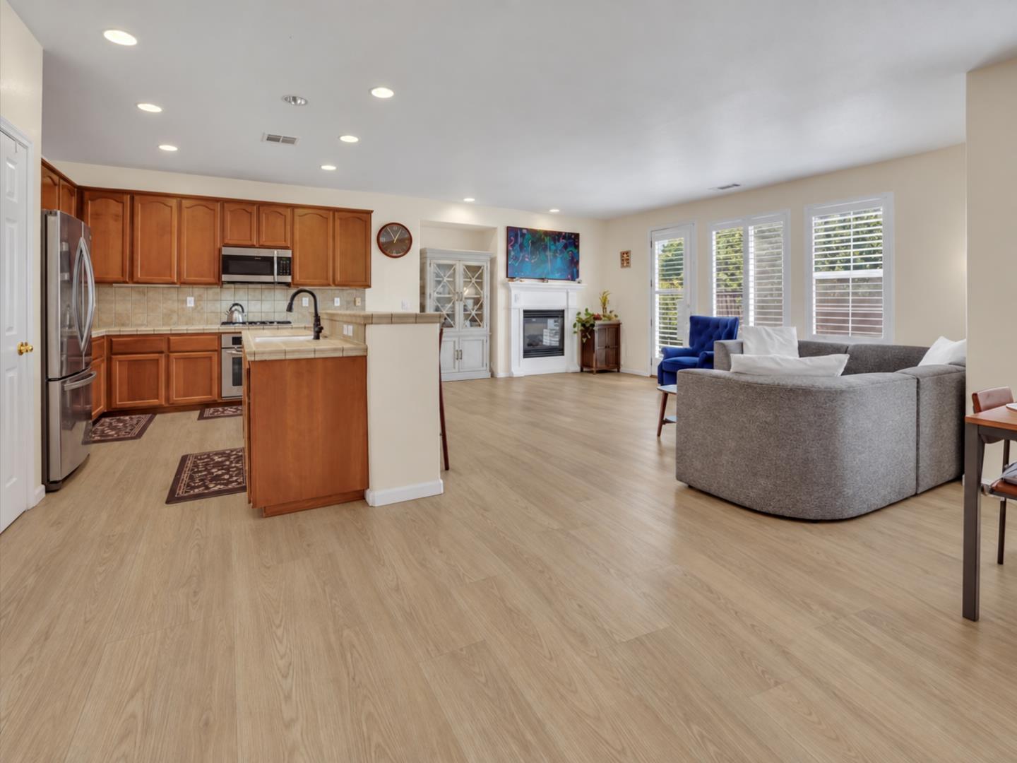 Open kitchen and living room with wood cabinets, a fireplace, and gray sectional sofa.