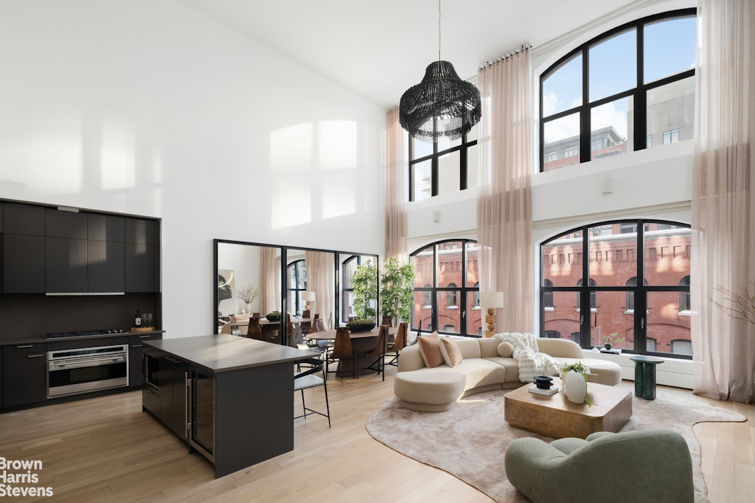 Loft living room and kitchen with double-height ceilings, arched windows, and a dark island.