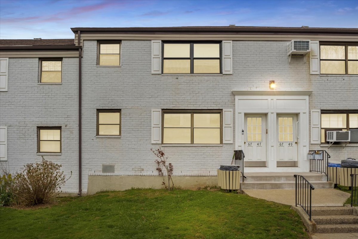 Two-story gray brick residential building with white entry doors and a small lawn at dusk.