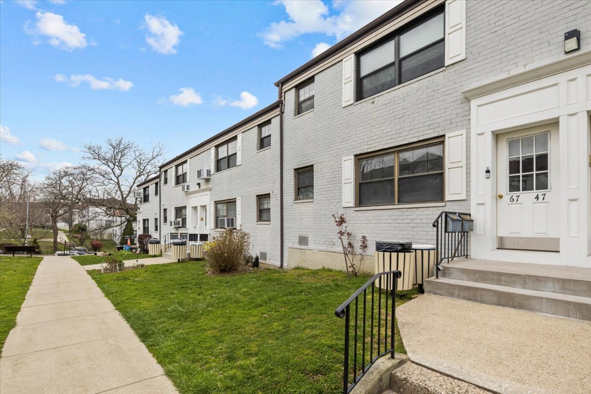 White brick residential row with a grassy lawn, concrete walkway, and entrance marked 67 and 47.