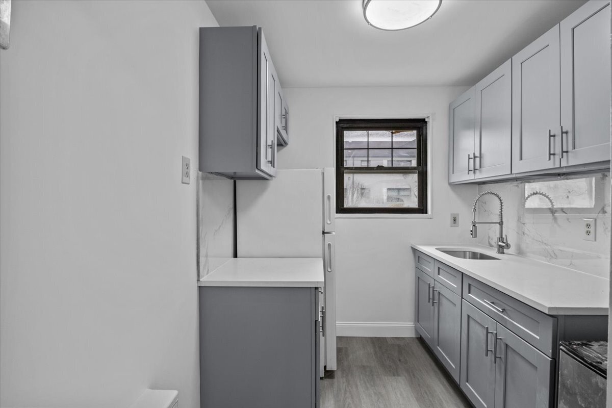 Renovated kitchen with gray cabinets, white countertops, marble-look backsplash, and a window above the refrigerator.