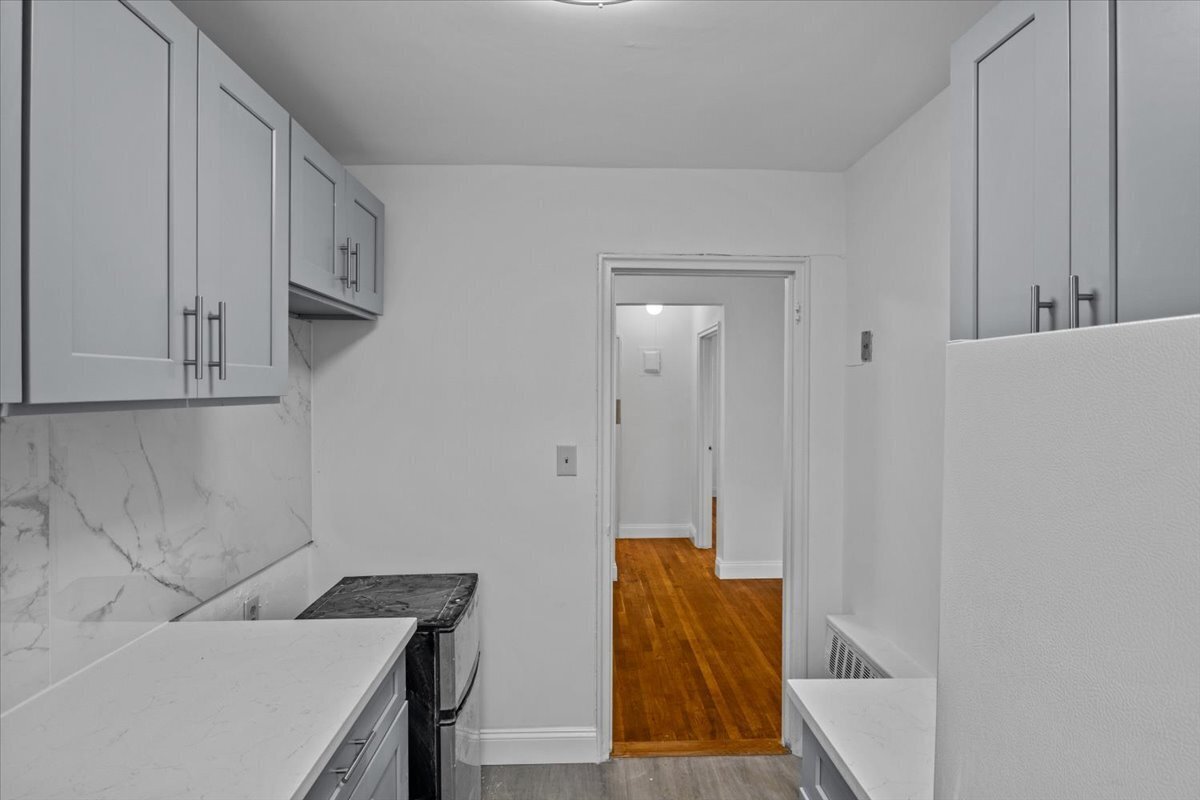 Narrow kitchen with white cabinets, marble-look counters and backsplash, and a dark range.