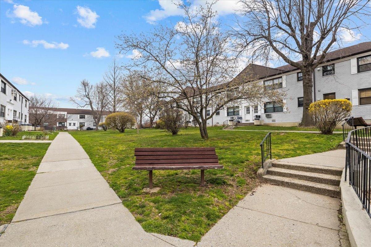 Apartment complex courtyard with a wooden bench, grassy lawn, concrete paths, and leafless trees.
