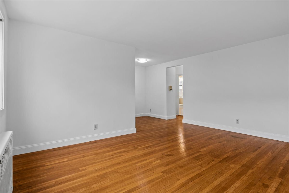 Empty room with polished hardwood floors, white walls, and an open doorway to an adjoining room.