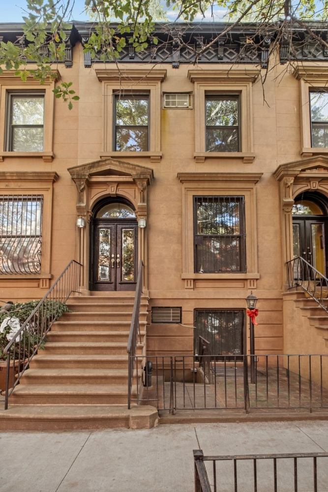 Brownstone townhouse with an ornate entrance, broad stone stoop, and iron railings.