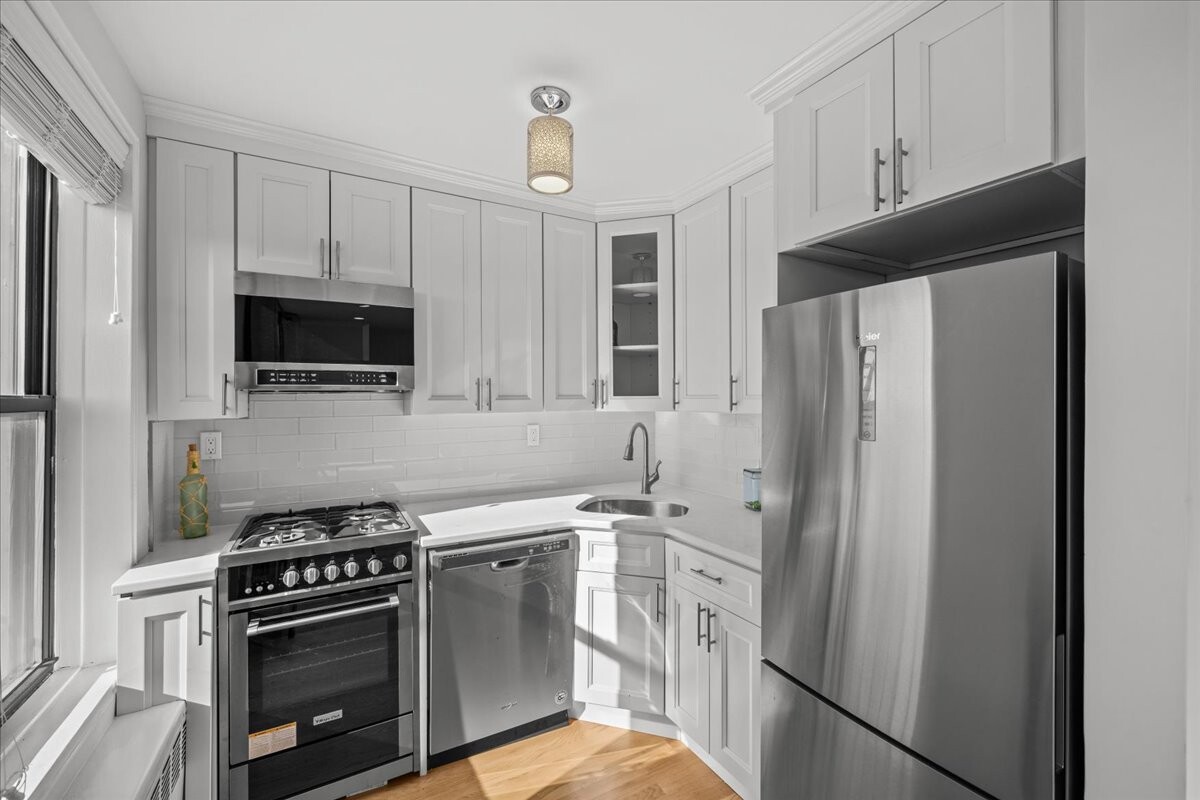 Bright kitchen with white shaker cabinets, stainless steel appliances, and sunlight streaming through a side window.