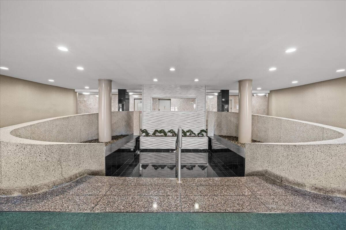 Apartment building lobby with curved terrazzo walls, glossy black floor, and a central planter.