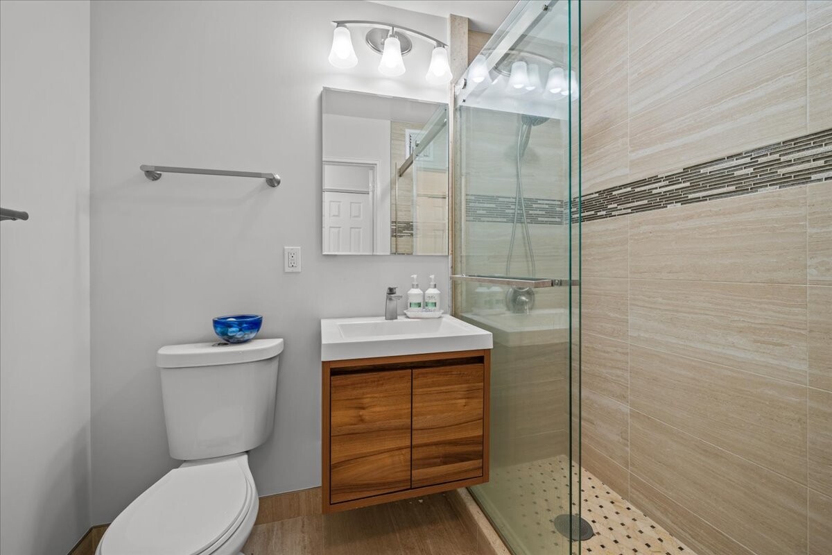 Modern bathroom with a wood vanity, white toilet, and glass-enclosed shower.
