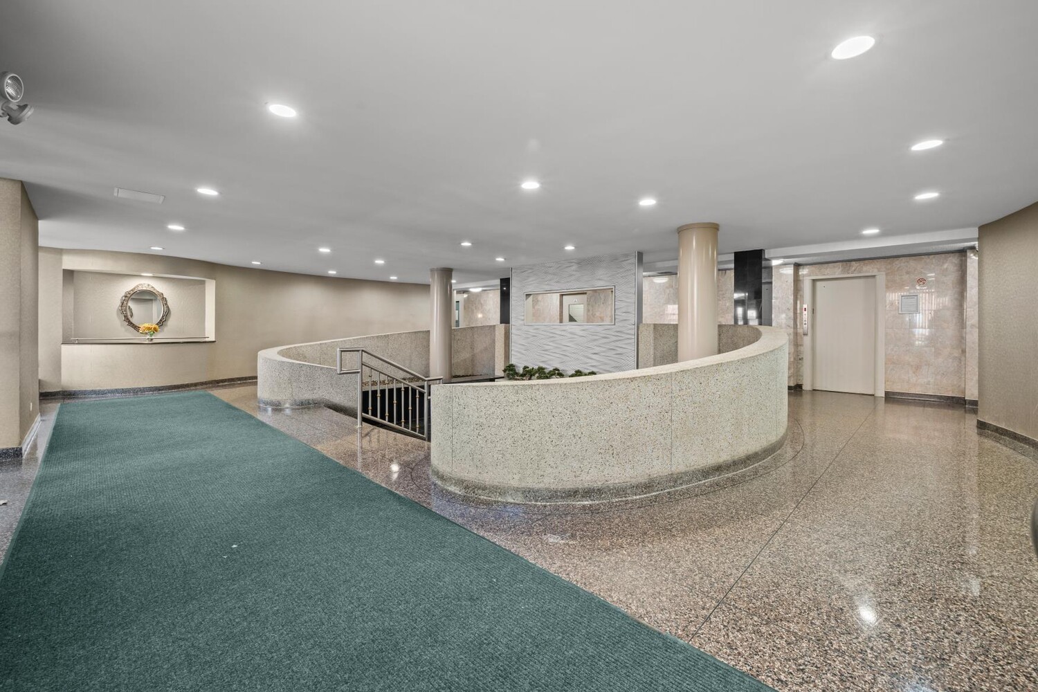 Apartment building lobby with a curved stone railing, elevator, and green carpet.