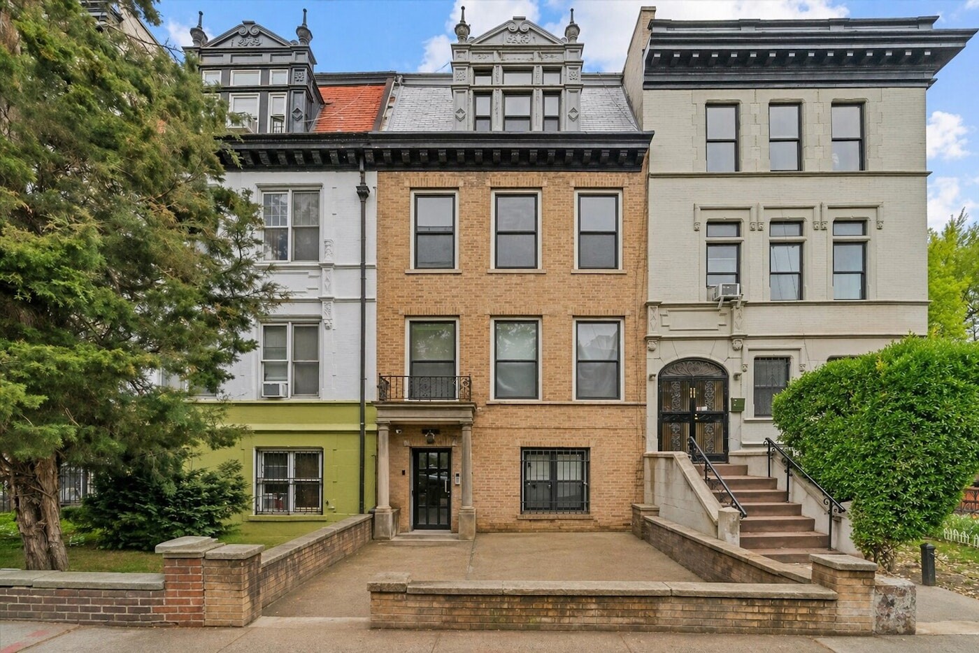 Brooklyn townhouse with an ornate mansard roof, front balcony, and brick-walled paved yard.