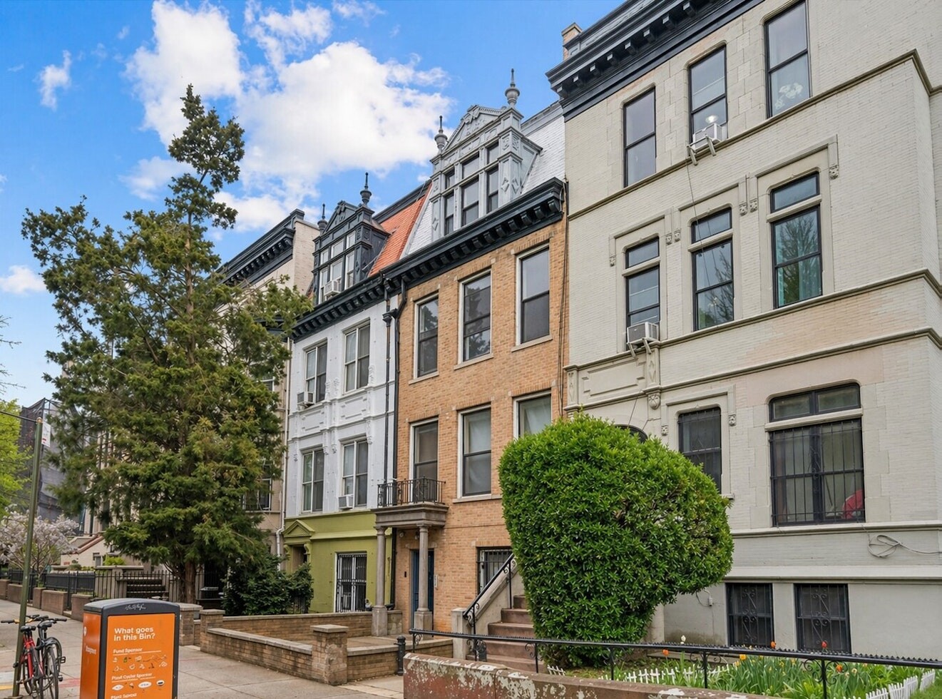 Attached Brooklyn townhouses with ornate cornices, brick facades, and leafy sidewalk landscaping.