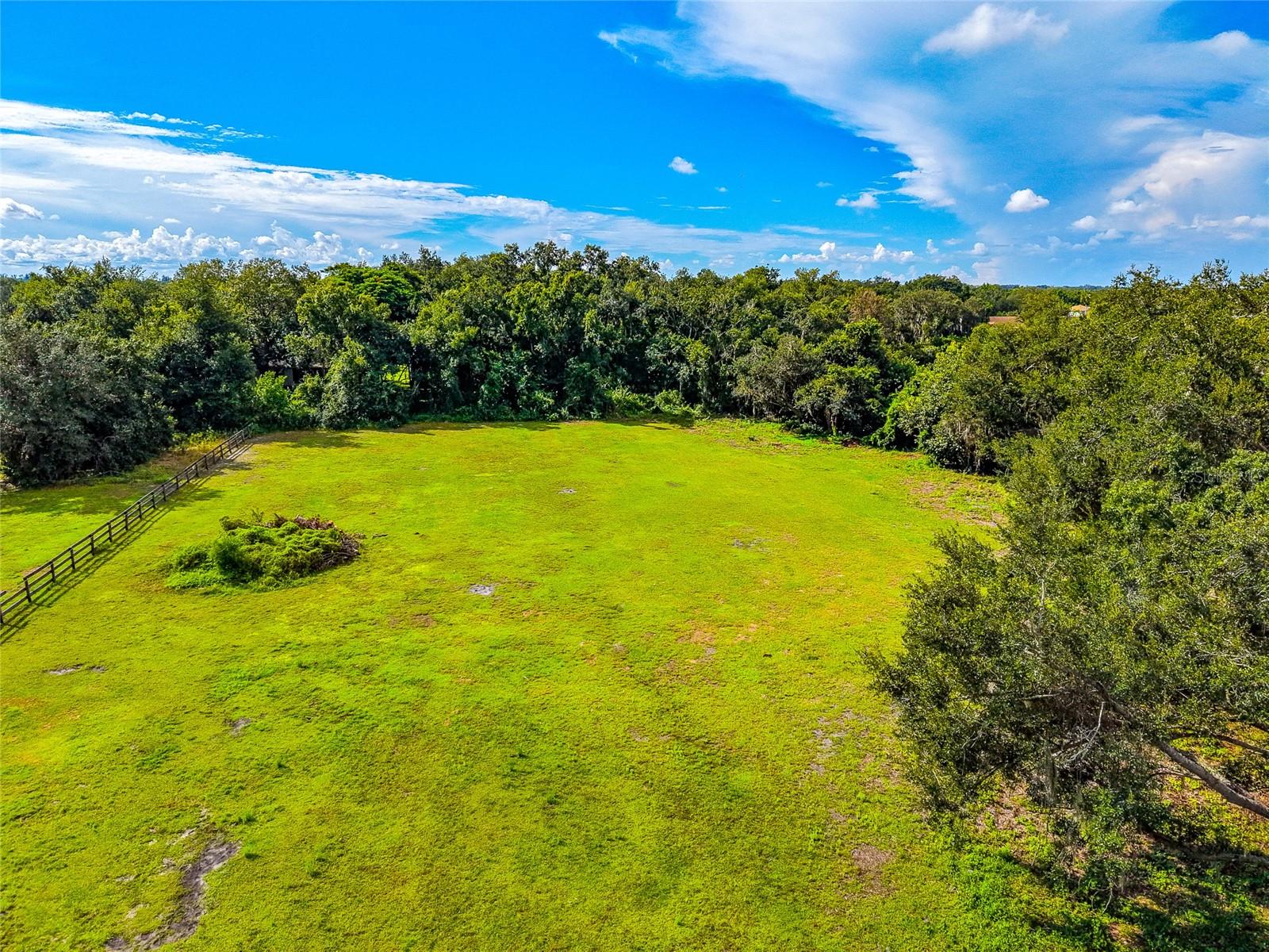 Aerial view of a grassy open lot bordered by trees, with a fence along one side.