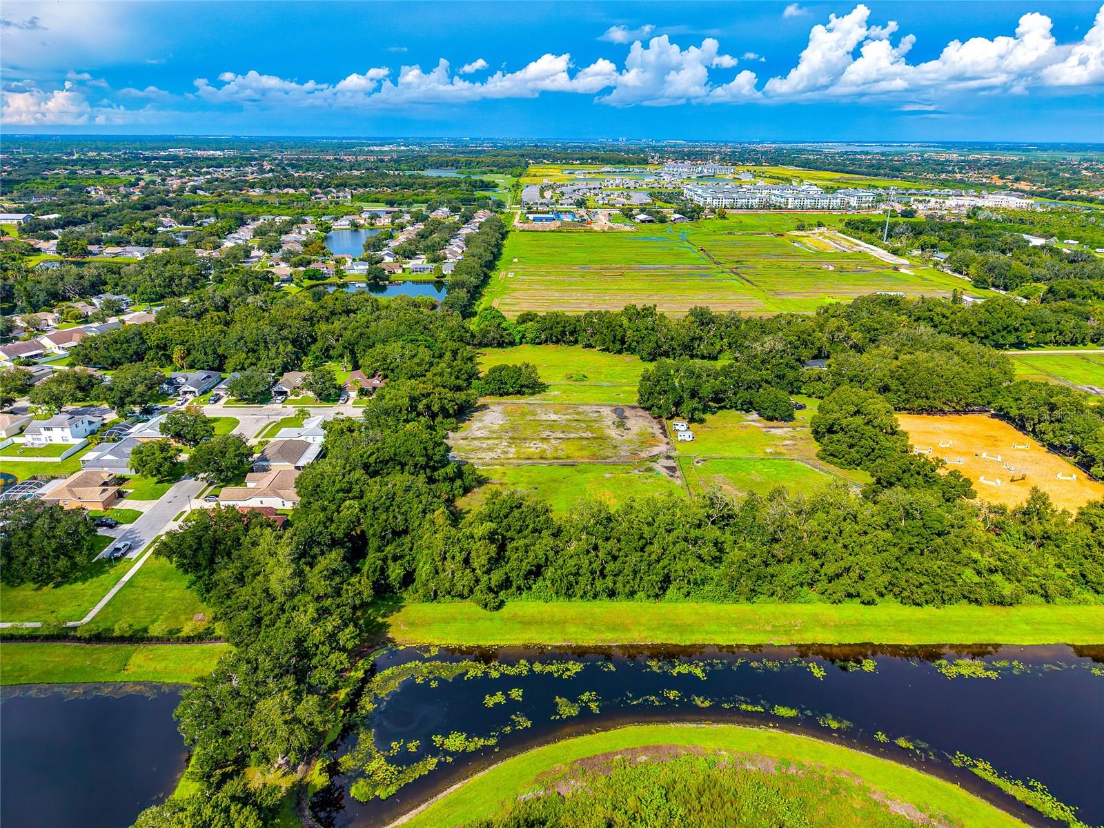 Aerial view of a grassy parcel beside a winding waterway, with homes and open fields nearby.
