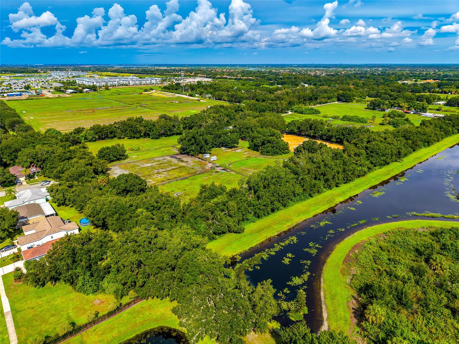 Aerial view of grassy, wooded land beside a winding waterway, with nearby homes and development in the distance.