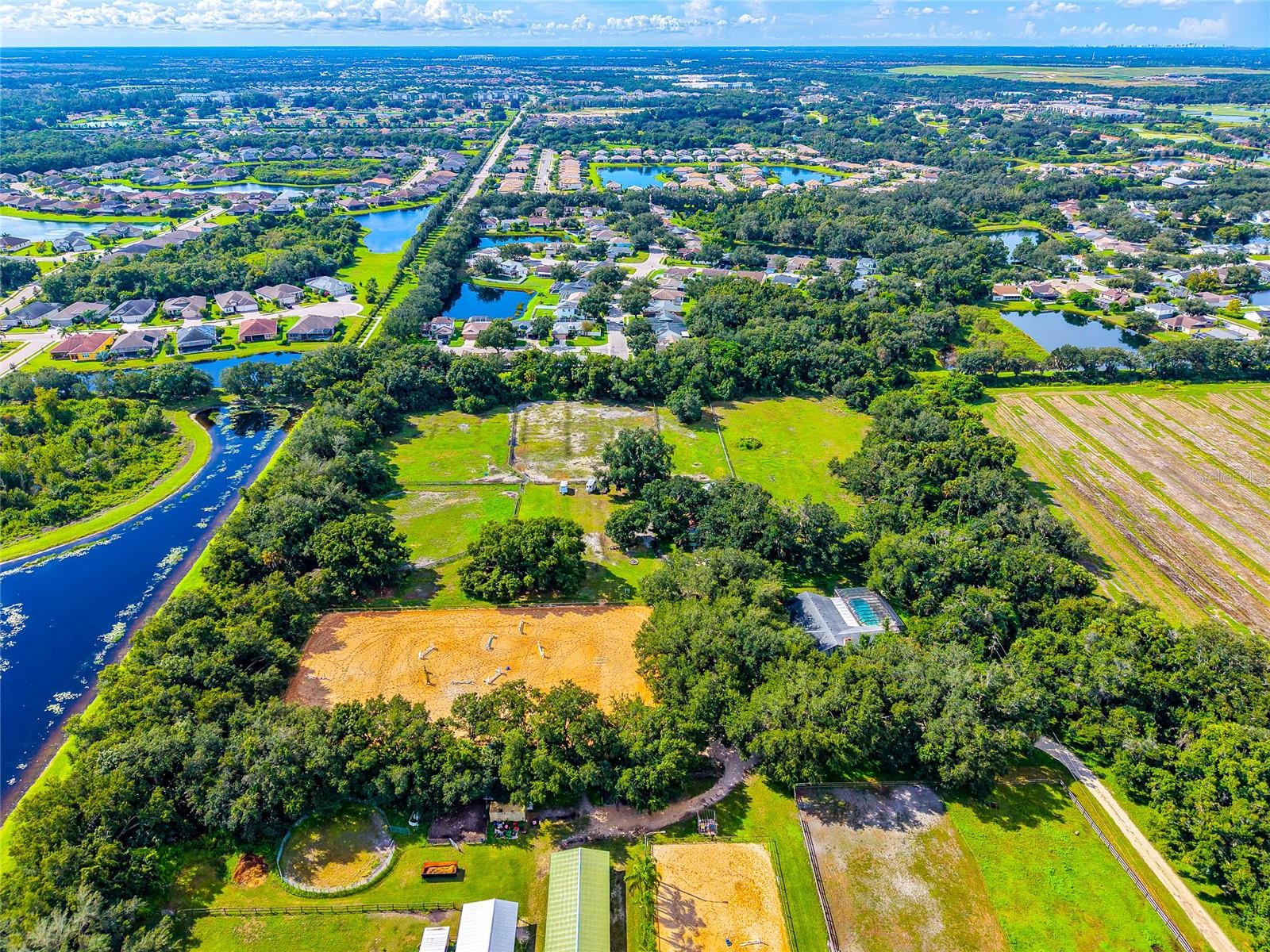 Aerial view of cleared land bordered by woods, ponds, paddocks, and nearby neighborhoods.
