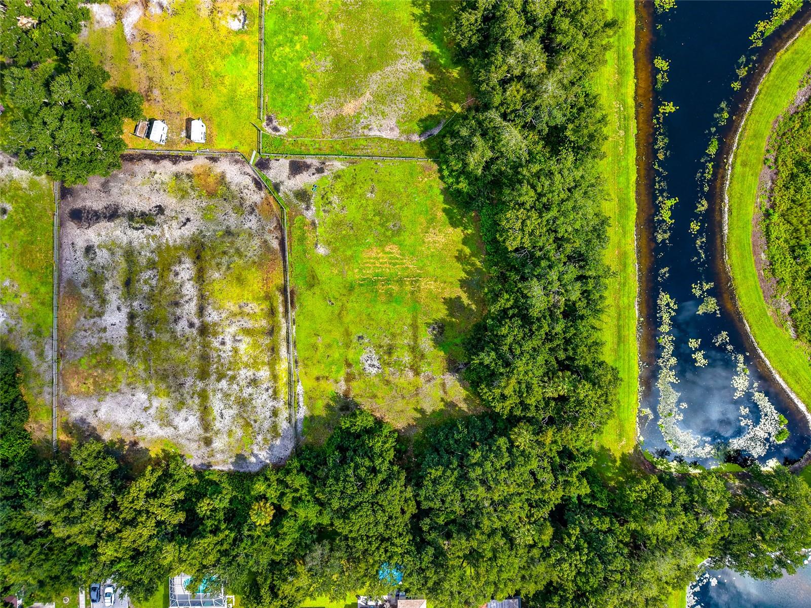 Aerial view of a cleared, fenced parcel beside a canal, surrounded by trees.