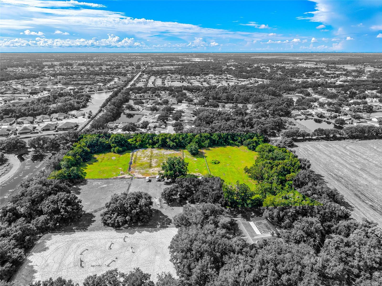 Aerial view of equestrian acreage with green fields and a sandy riding arena.