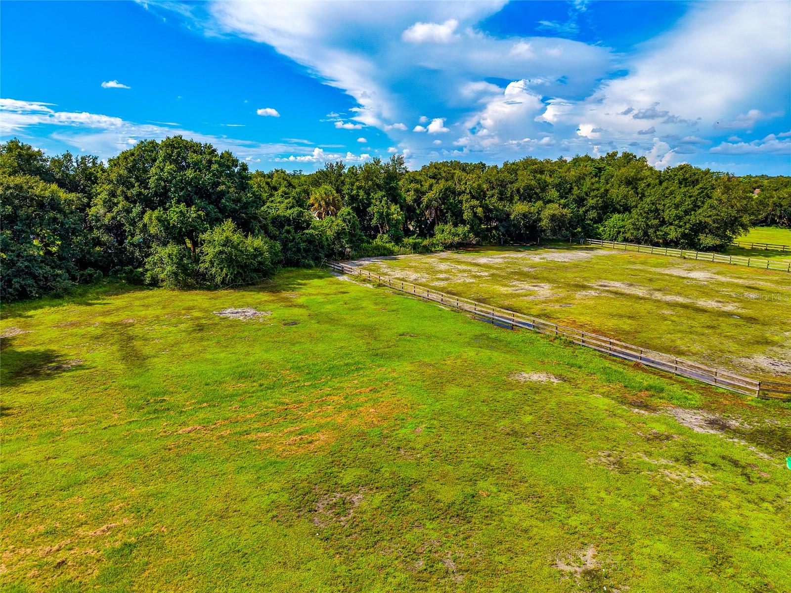 Aerial view of a broad grassy parcel bordered by trees and a wooden fence.