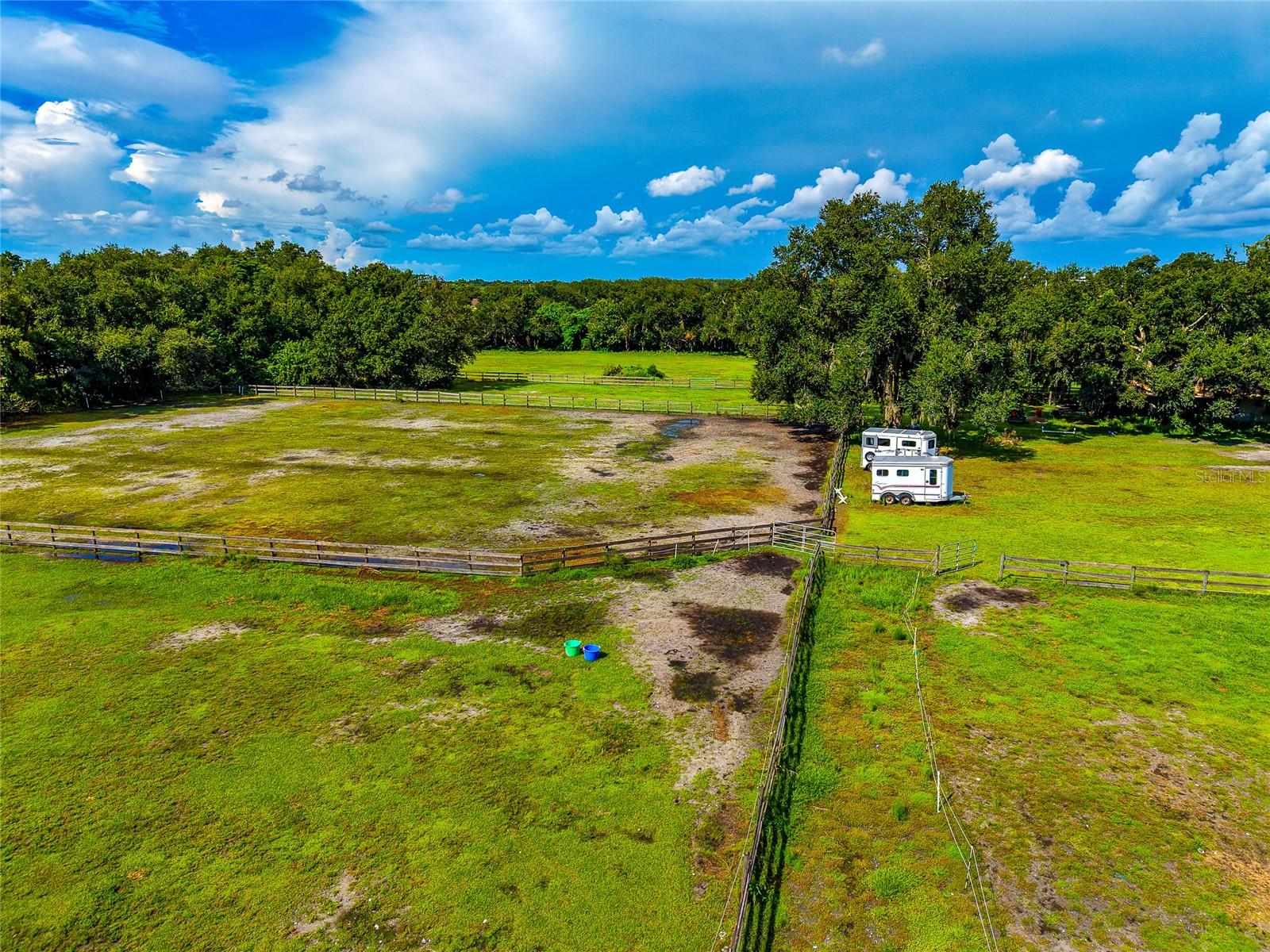 Fenced pasture with several paddocks, mature trees, and two horse trailers.