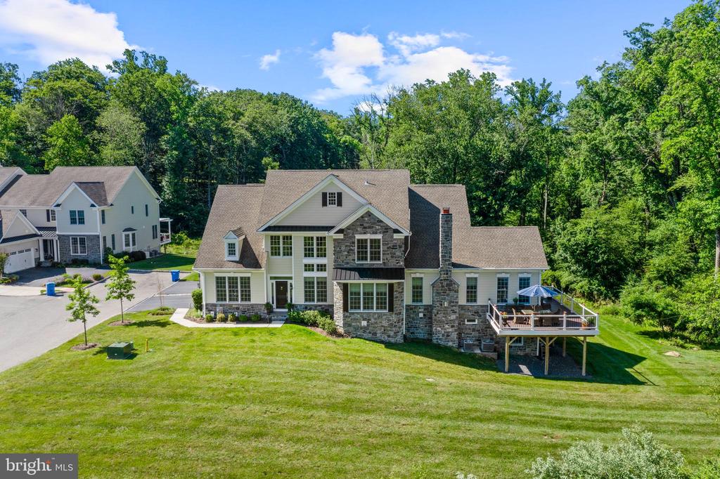 Two-story stone house with a raised deck and broad lawn bordered by mature trees.