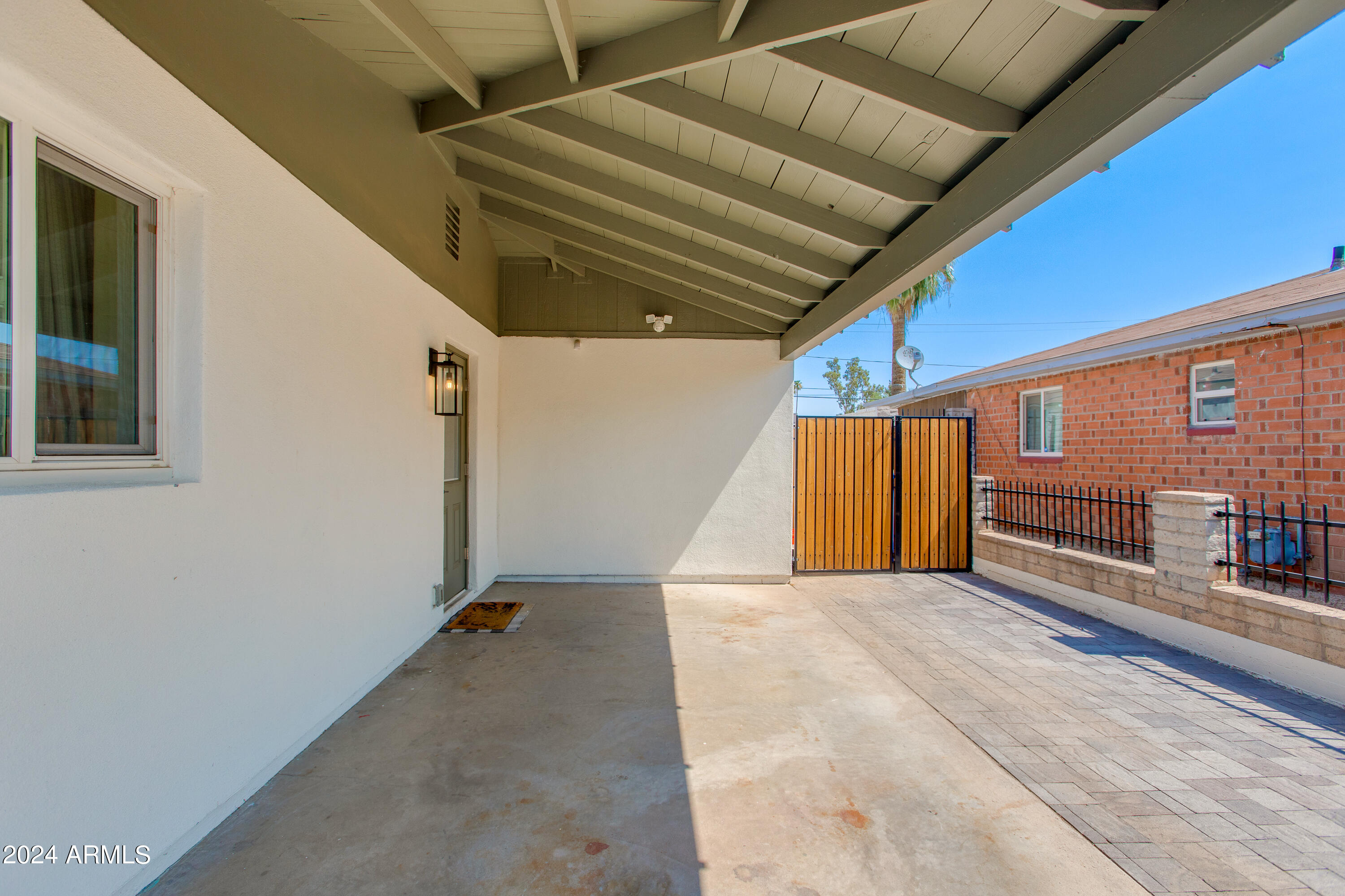 Covered patio with exposed beams, paver flooring, and a wooden privacy gate.