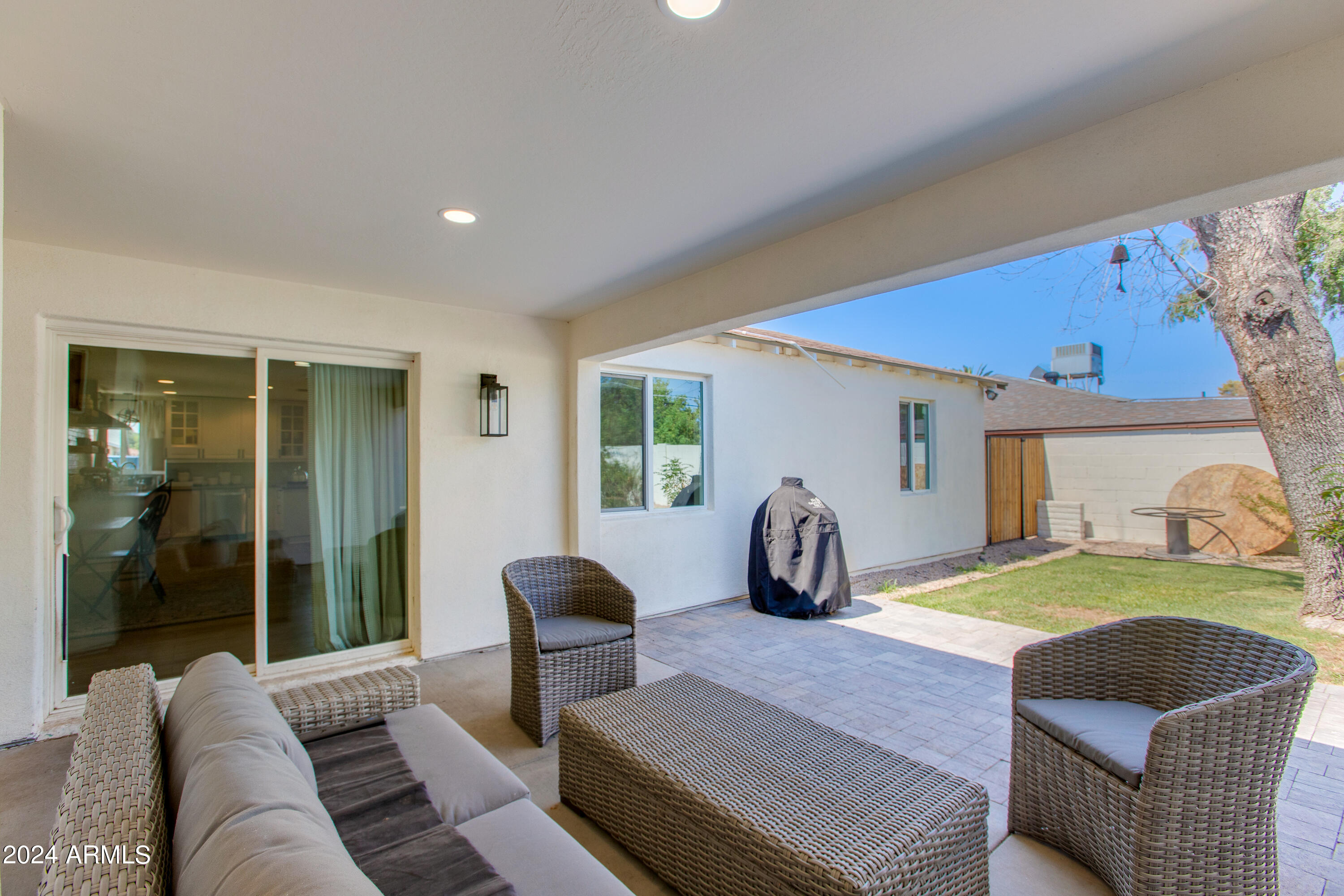 Covered patio with wicker seating opens onto a paved terrace and grassy backyard.