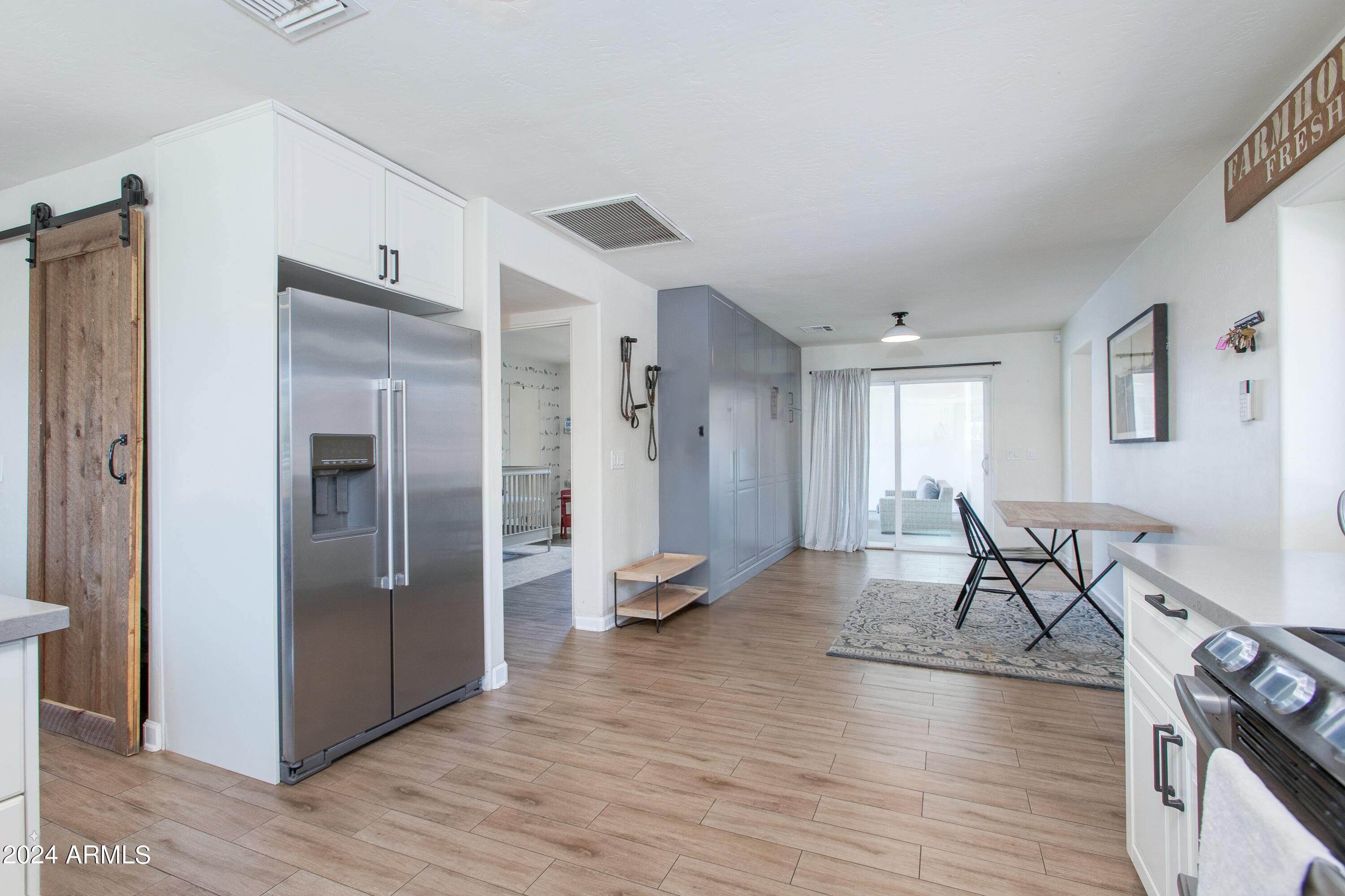 Kitchen and dining area with stainless steel refrigerator, gray cabinets, wood-look floors, and sliding glass doors.
