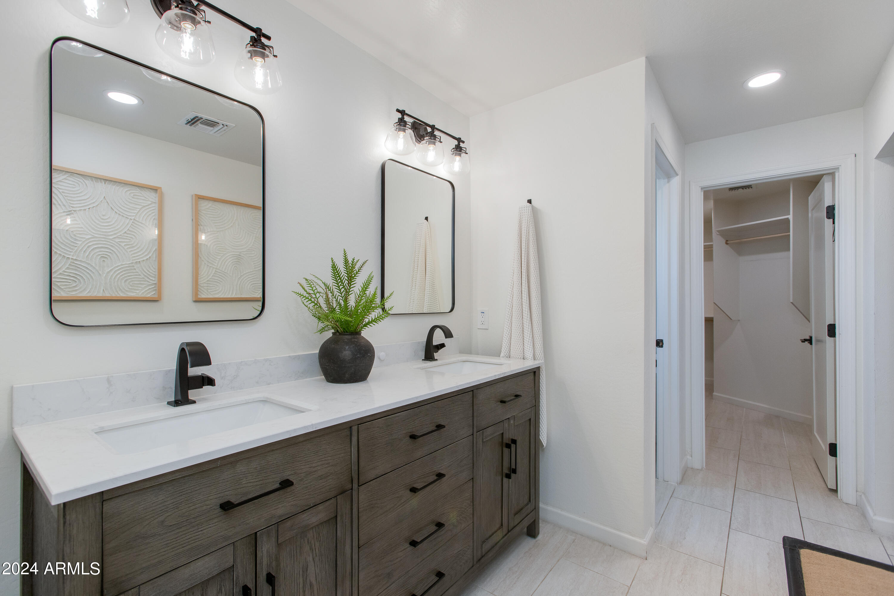 Bathroom with a dark wood double vanity, two sinks, black faucets, and an open walk-in closet.