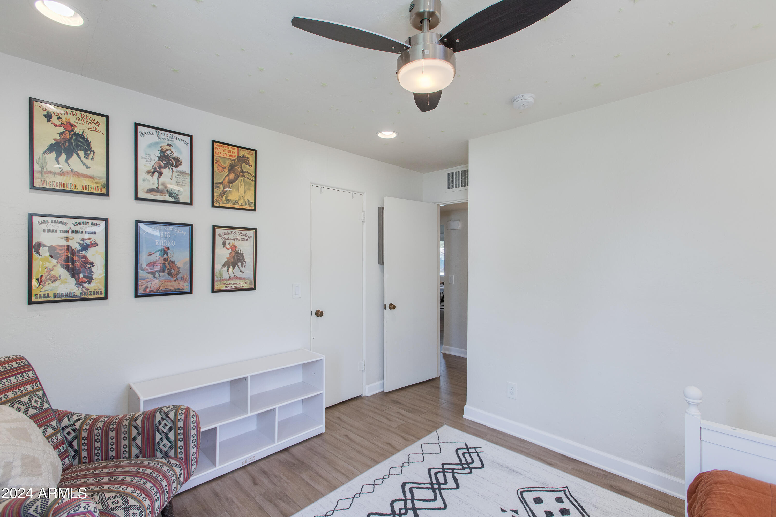 Bedroom with framed rodeo posters, a patterned armchair, and a ceiling fan.