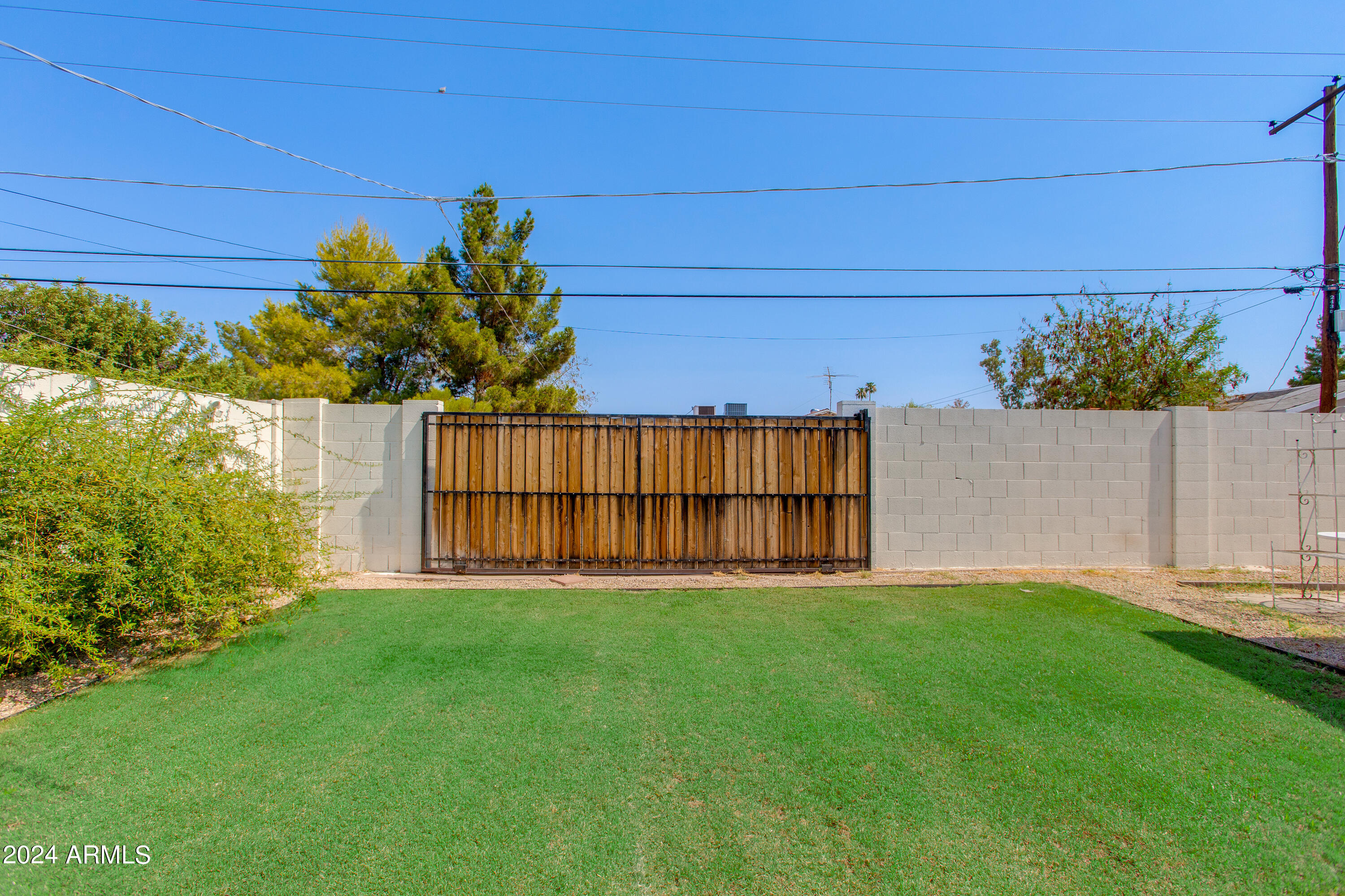 Backyard lawn bordered by a block wall and wooden sliding gate.