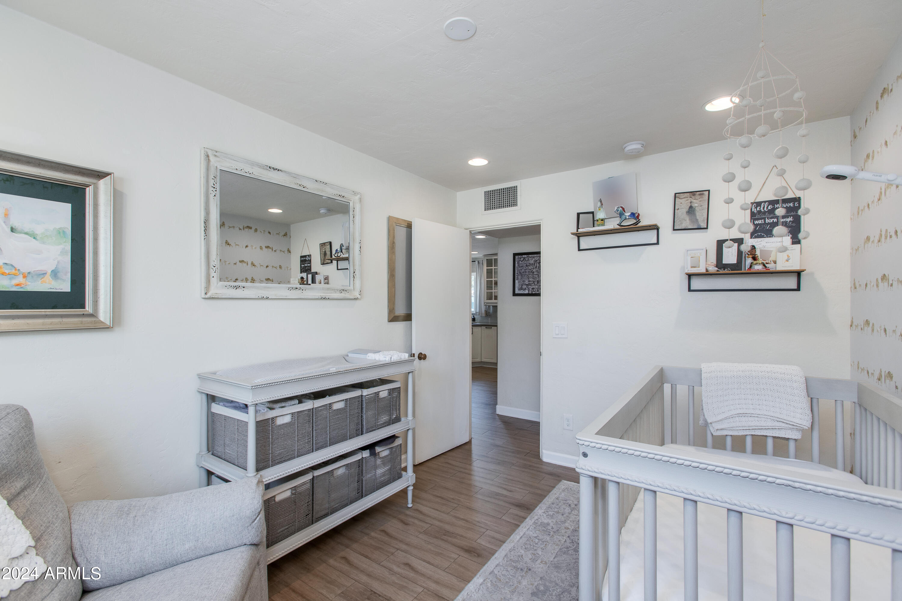 Nursery with a white crib, changing table with storage baskets, and gray armchair.