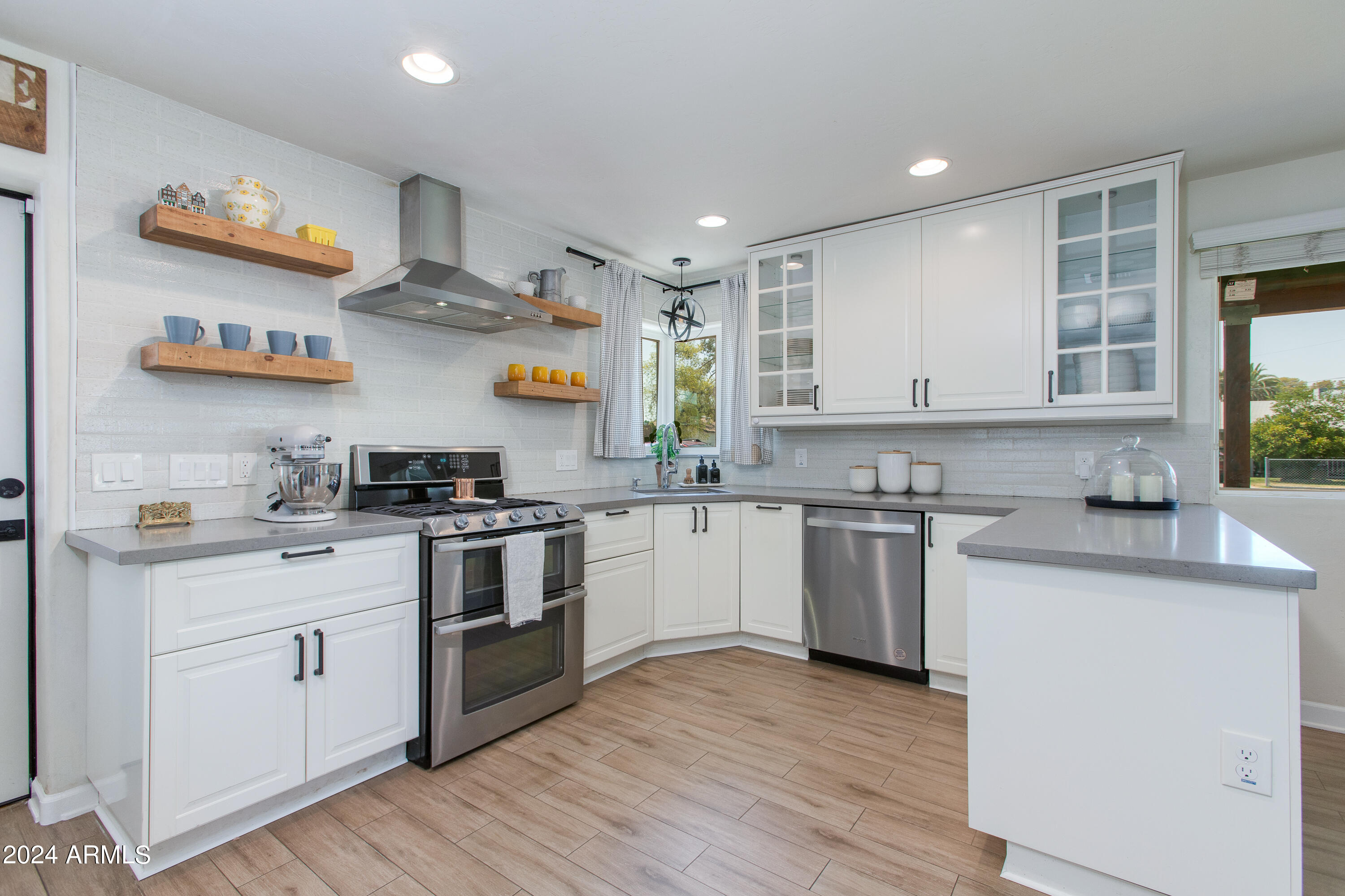 Bright white kitchen with open wood shelves, stainless steel appliances, and a large peninsula.