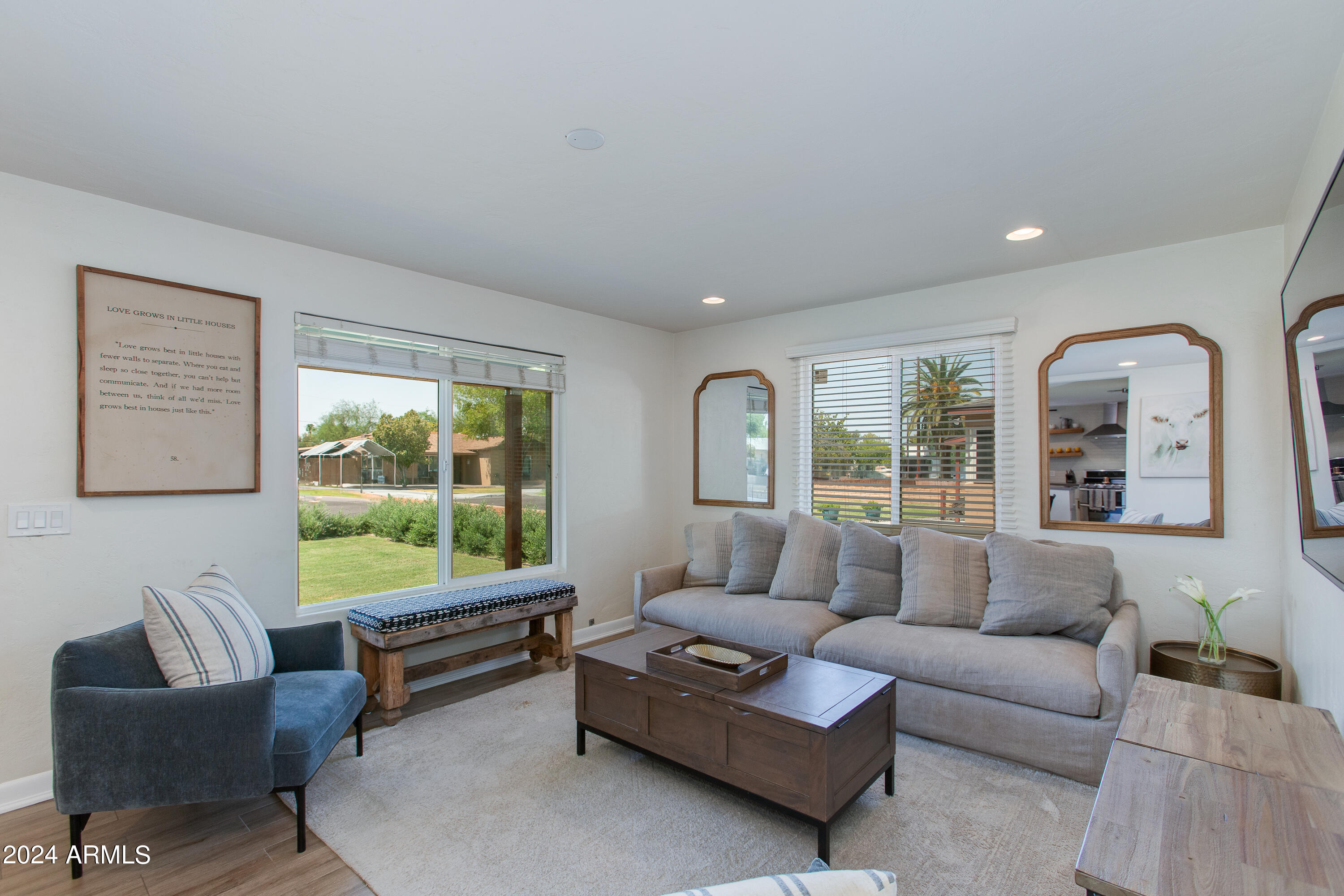 Living room with a gray sofa, blue armchair, wooden coffee table, and large windows overlooking a green yard.