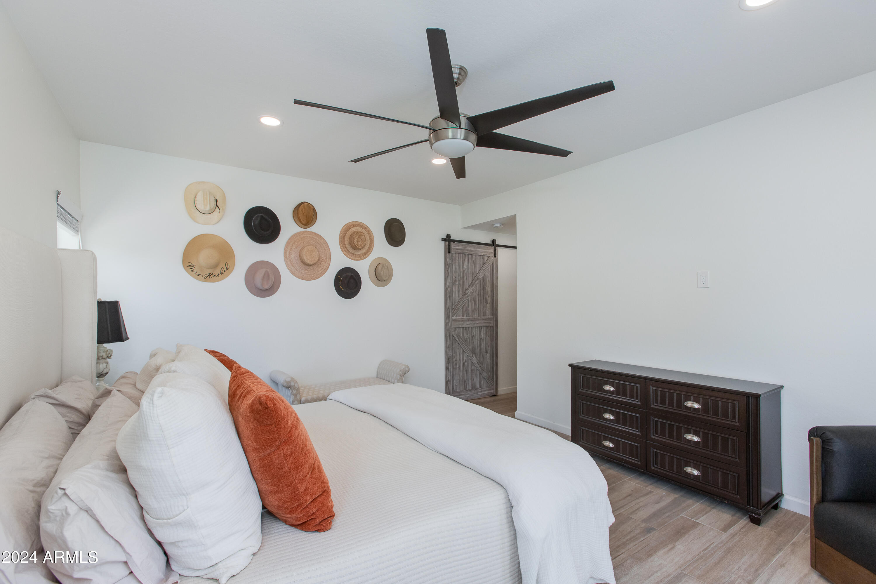 Bedroom with white bedding, rust accent pillows, decorative hats, and a dark wood dresser.