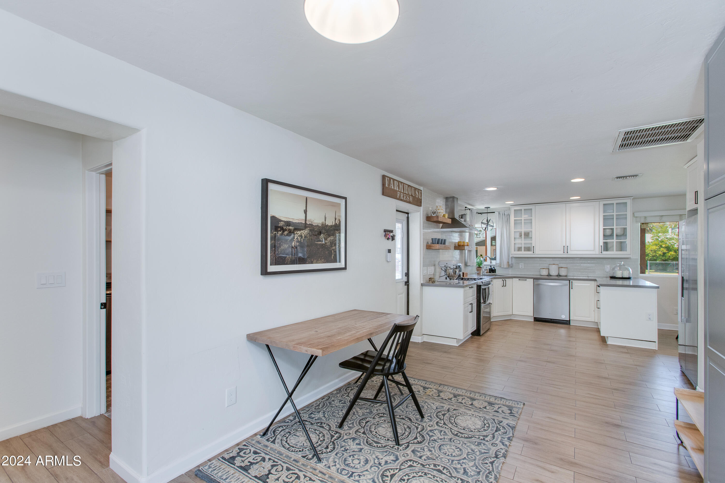 Open-plan kitchen with white cabinets and stainless appliances, with a wood table and patterned rug.