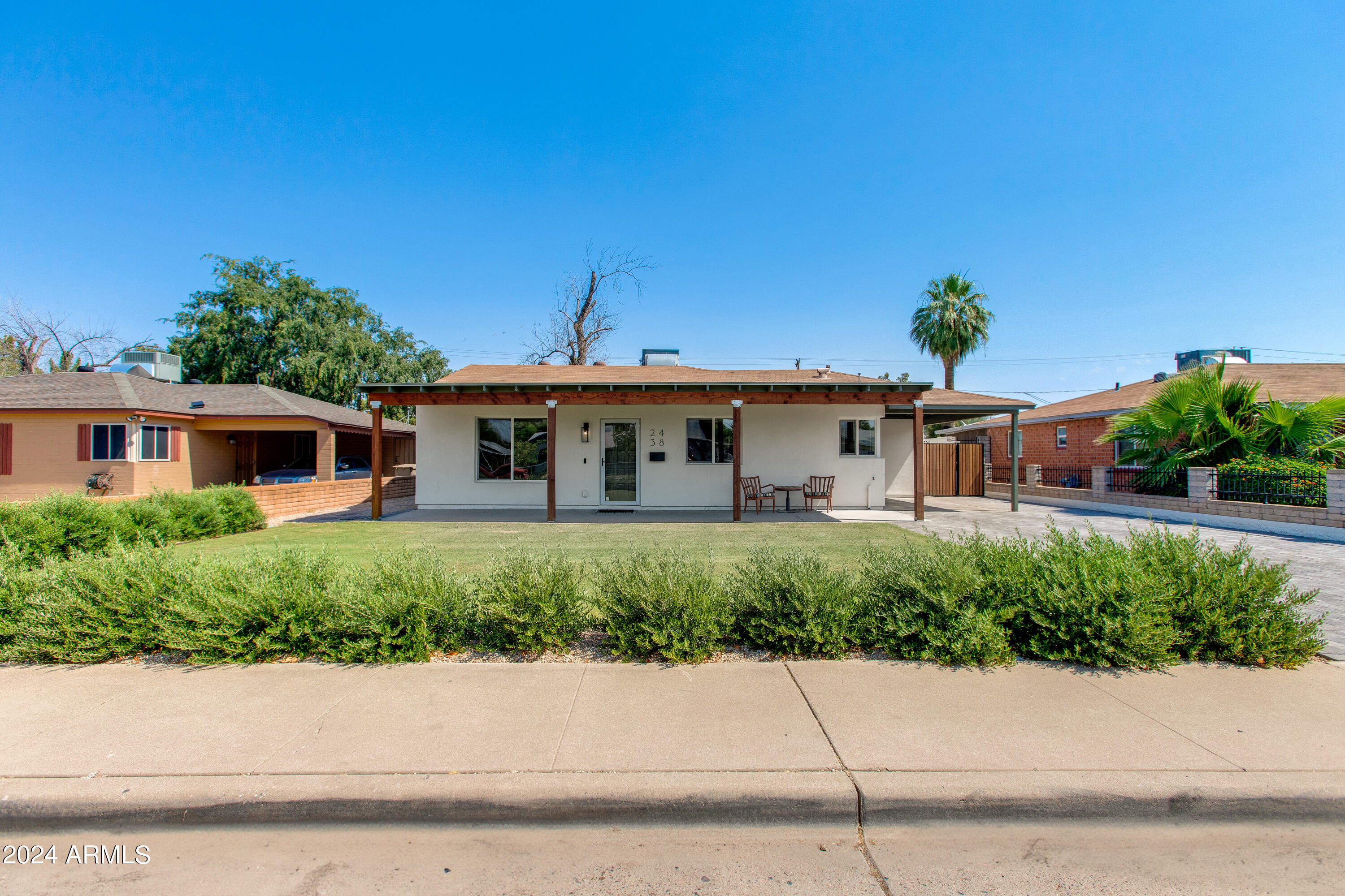 Single-story white home with a broad covered porch, front lawn, and palm trees.
