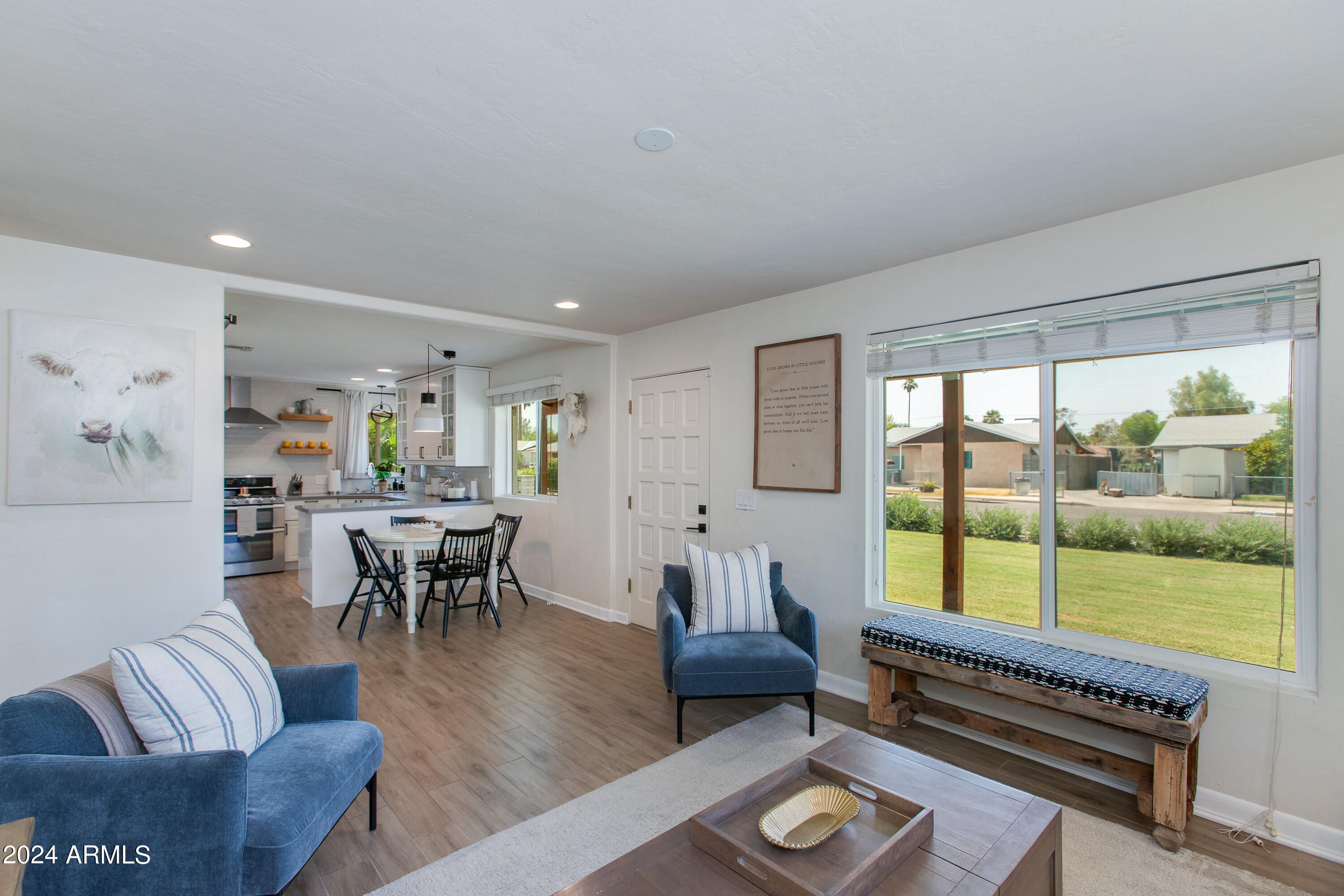 Open-plan living room with blue seating, dining area, and large window overlooking the lawn.