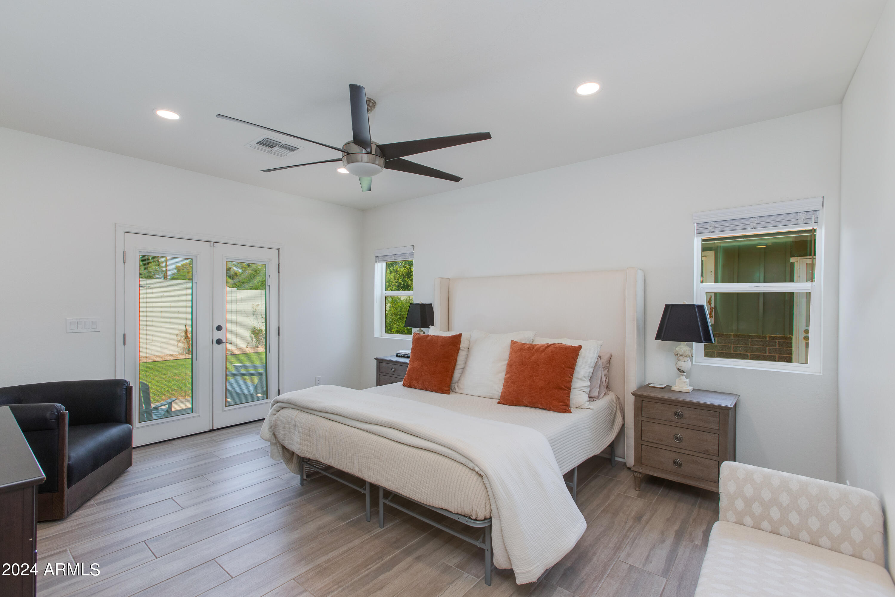 Furnished bedroom with a large white bed, rust-colored pillows, and glass doors to a patio.