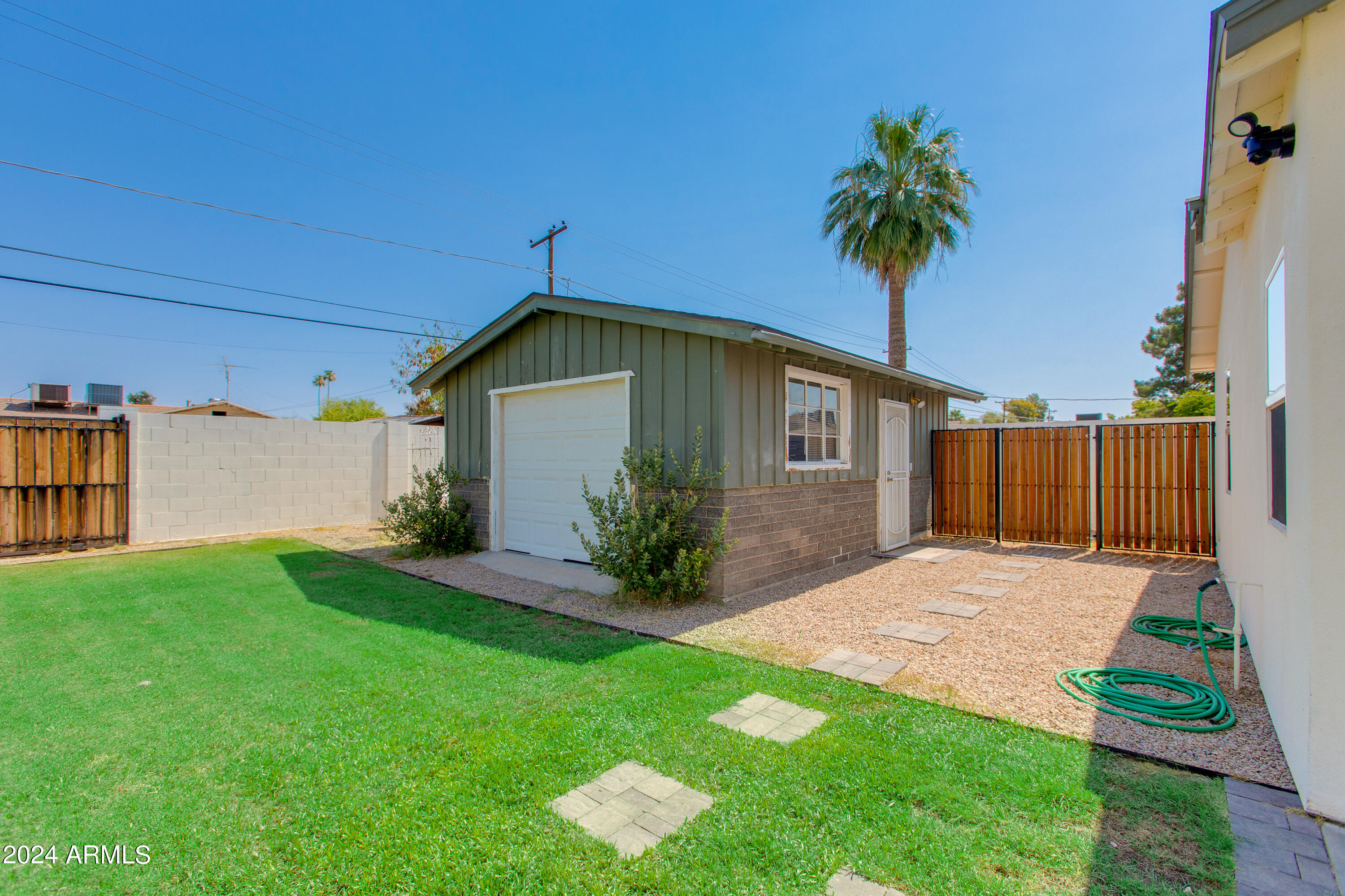 Backyard with a detached garage, green lawn, stepping stones, and a wooden gate.