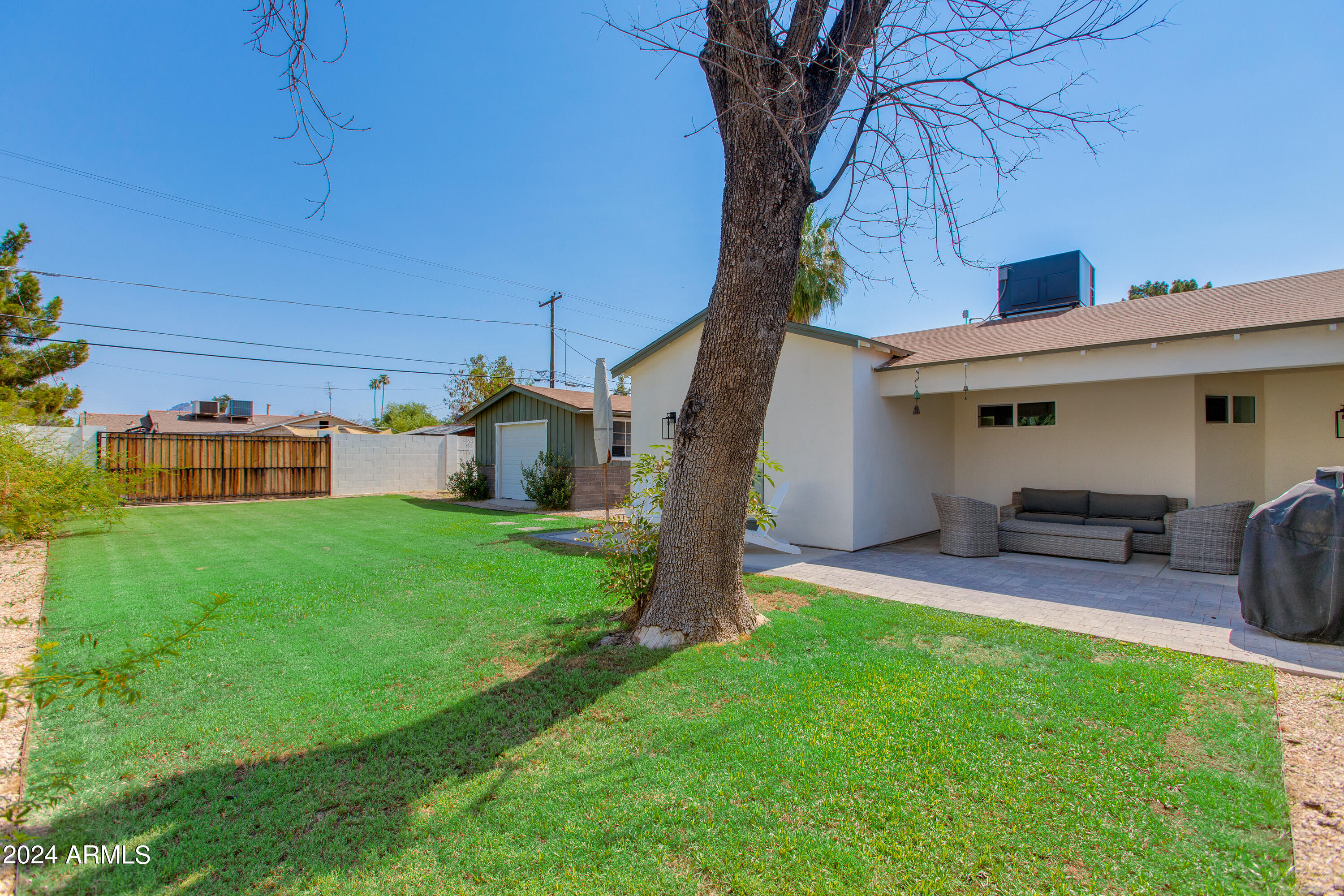 Backyard with a large shade tree, green lawn, and covered patio with outdoor seating.
