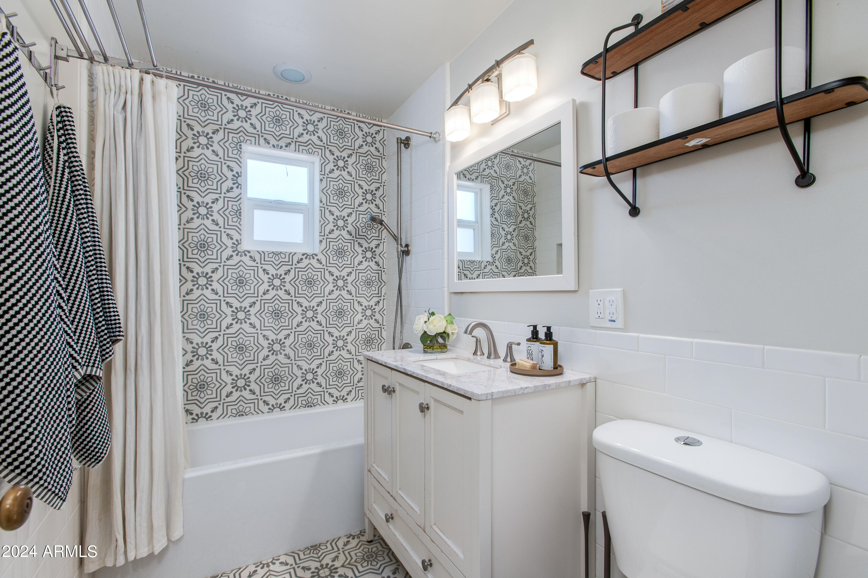 Bathroom with patterned tile shower wall, white vanity, and wood-and-metal wall shelves.