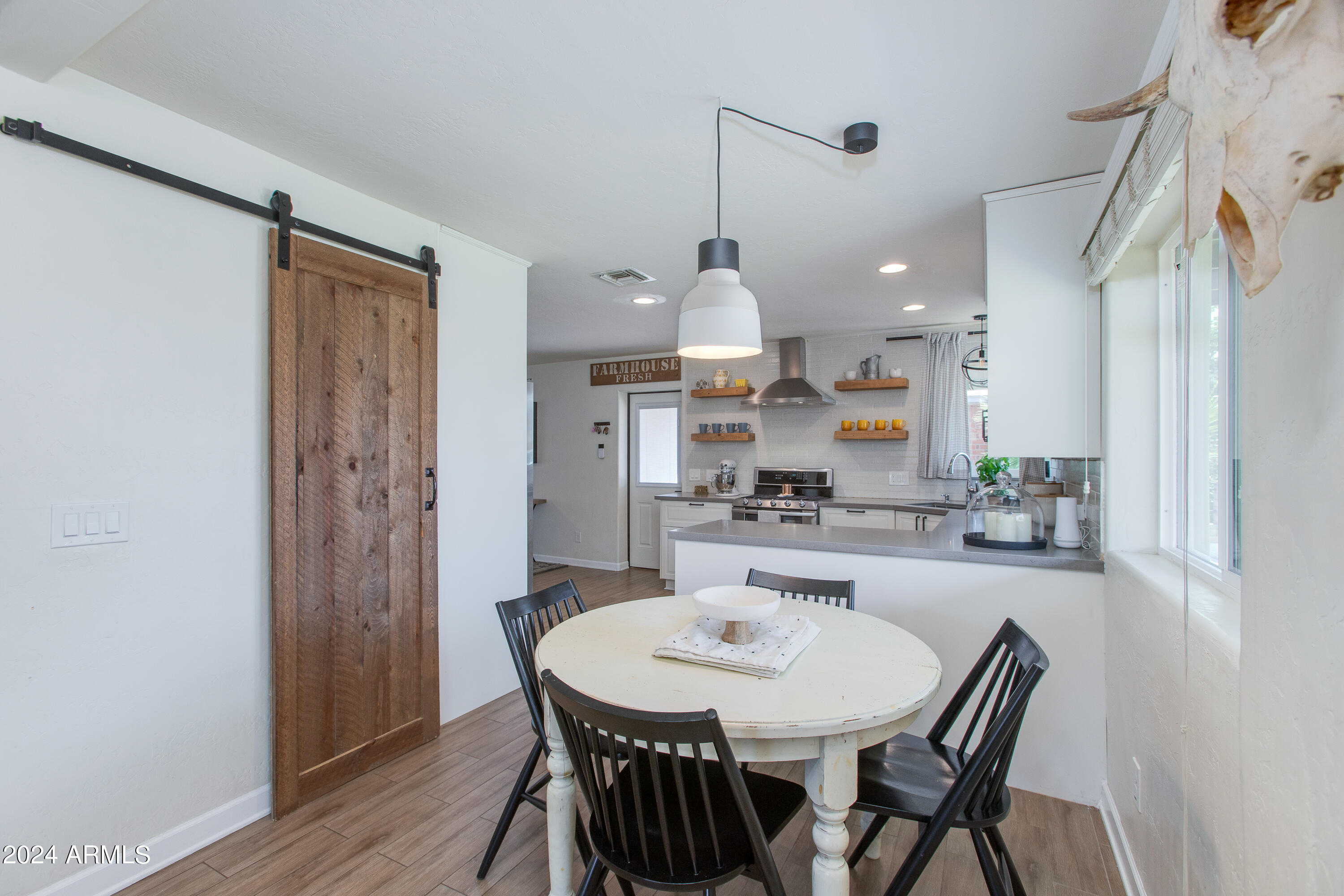 Dining area with round white table and black chairs beside a rustic barn door and open kitchen.