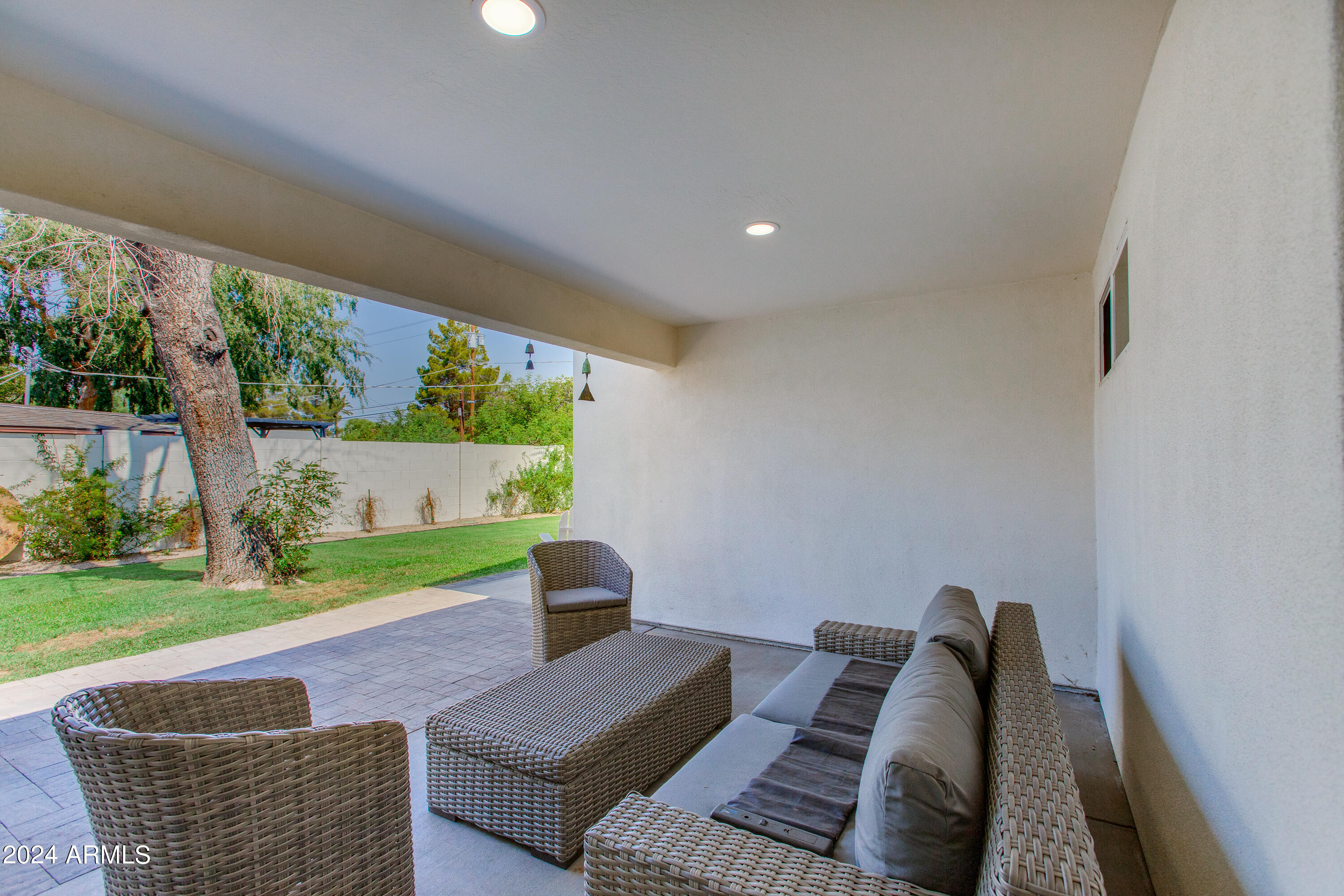 Covered backyard patio with wicker seating overlooking a lawn and mature tree.
