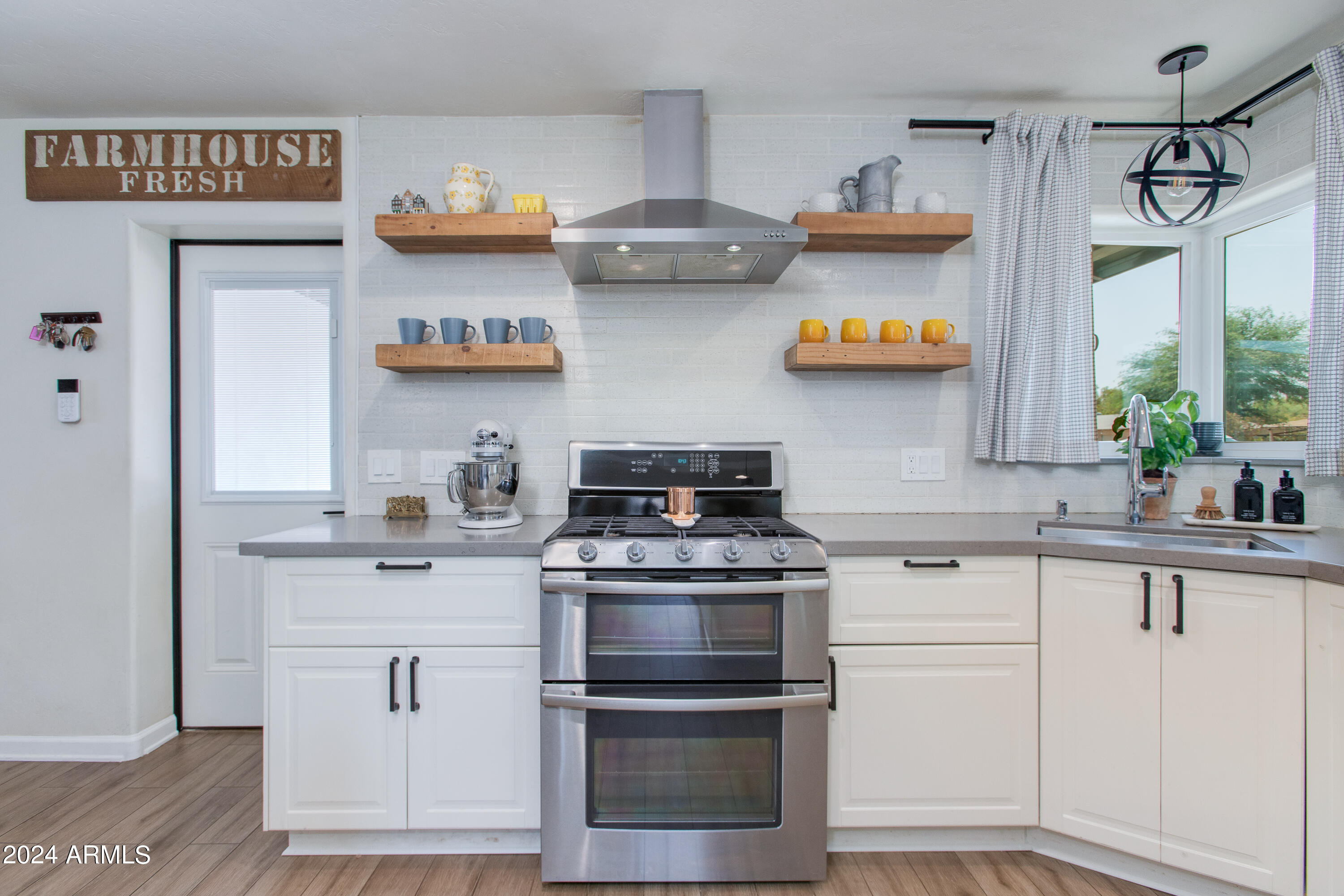 Kitchen with white cabinets, open wood shelves, and a stainless-steel range beneath a metal hood.