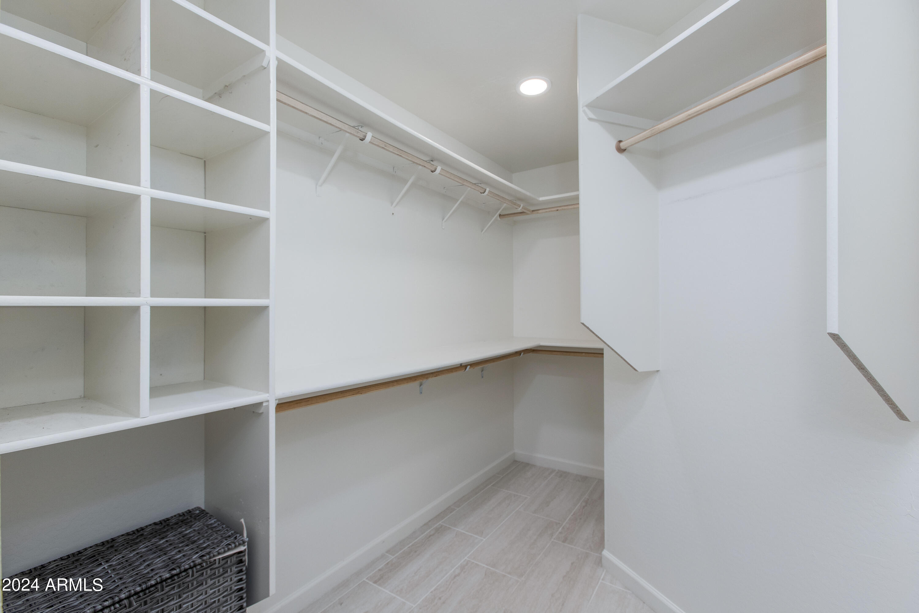 Walk-in closet with built-in shelving, several hanging rods, and a light tile floor.