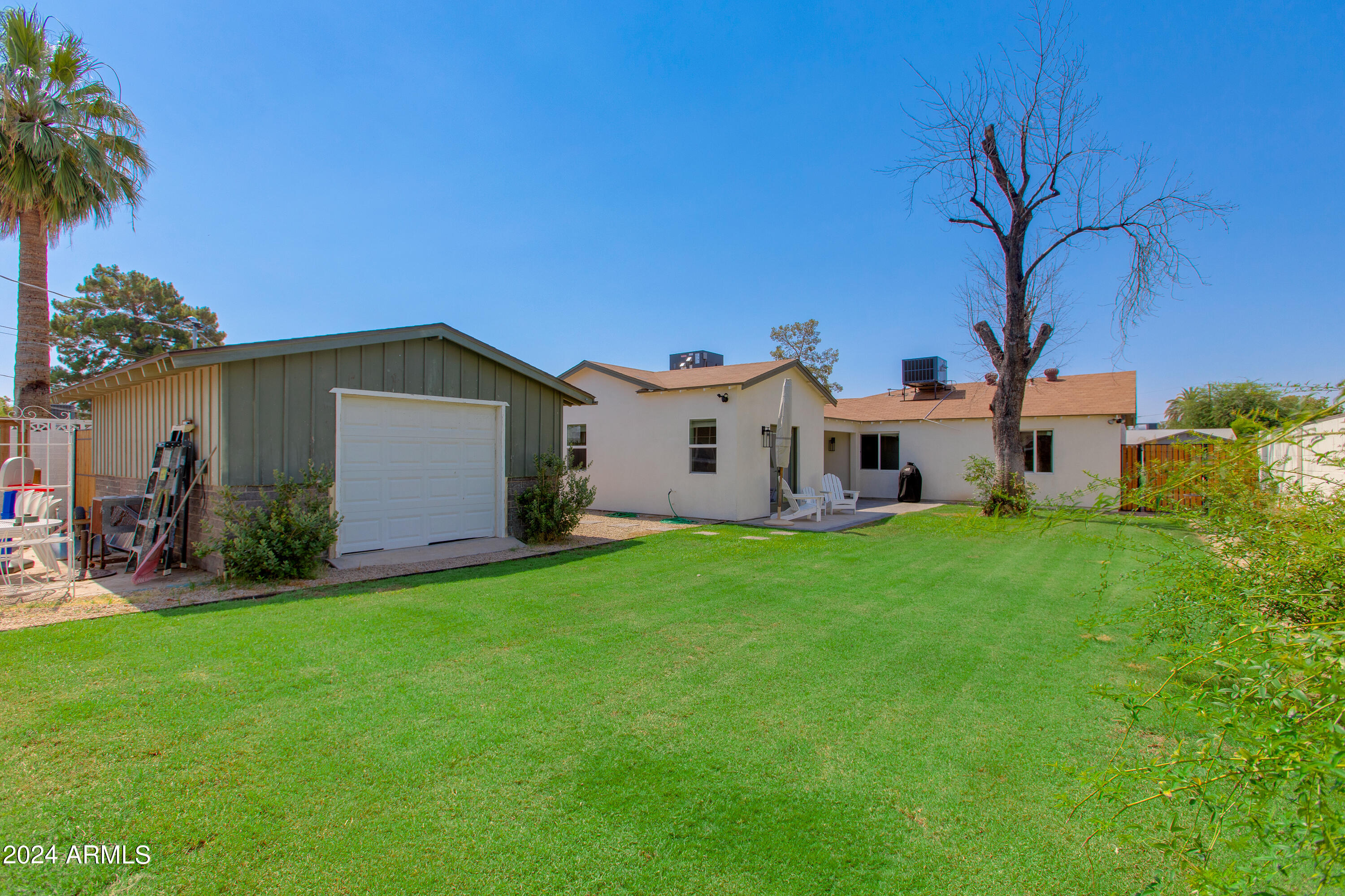 Backyard with a detached garage, broad lawn, and patio beside a single-story home.
