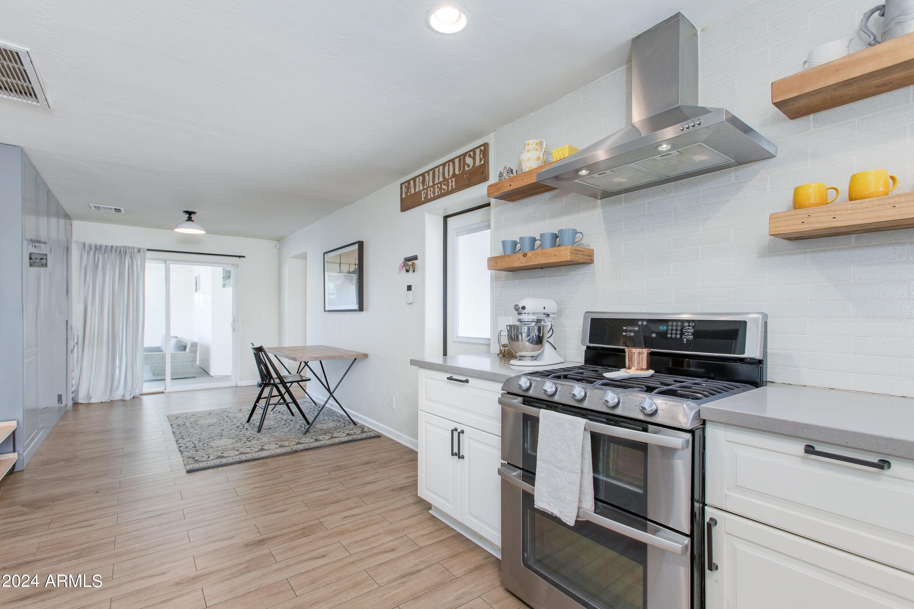 Kitchen with stainless steel range, white tile backsplash, open wood shelves, and a small dining nook.